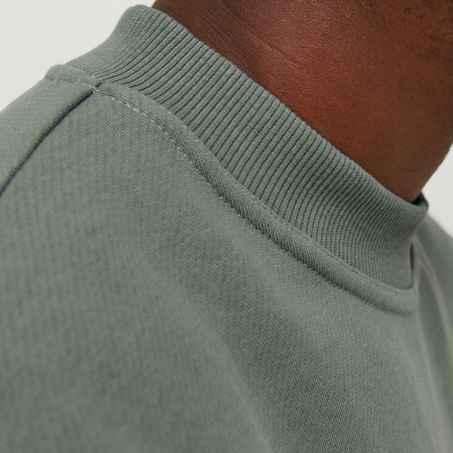 Gola alta canelada de camisola cinza esverdeada em detalhe num pescoço castanho.