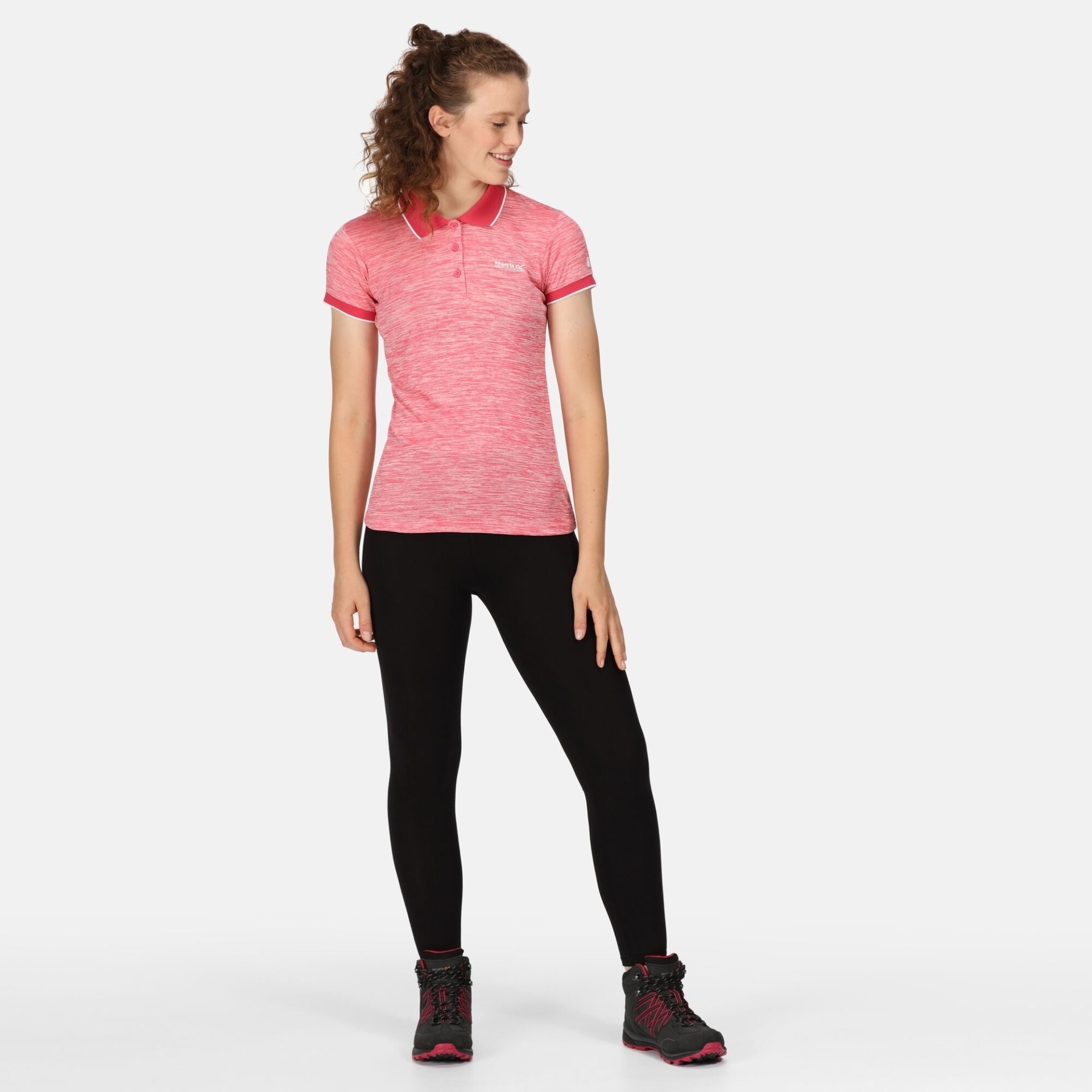 Mulher com polo rosa, calças pretas e botas de caminhada cinzentas e rosa