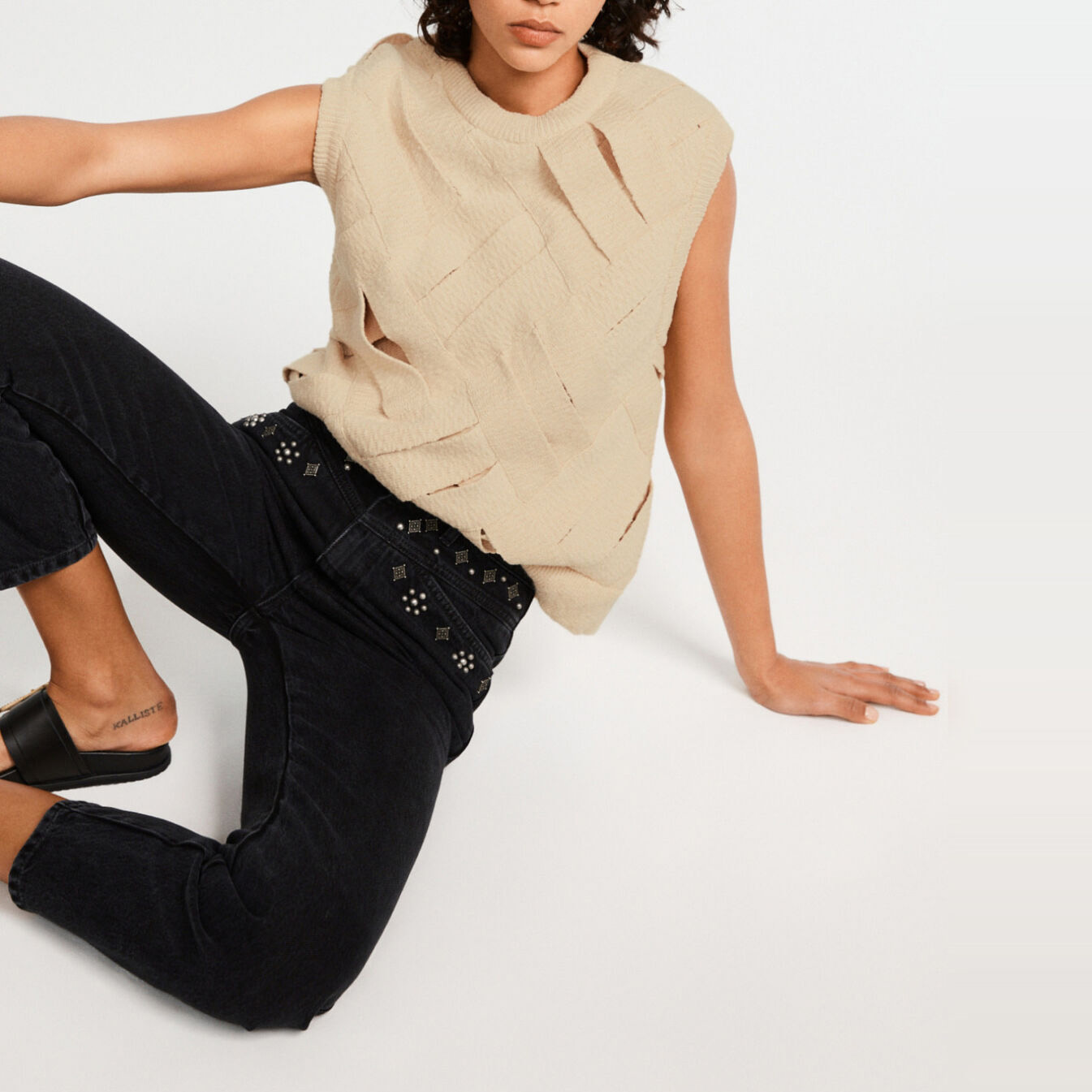 Top bege recortado, calças pretas com tachas e sandálias pretas