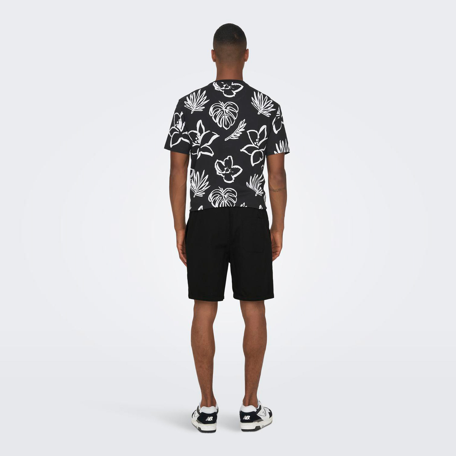 Homem de costas com camisola preta estampada, calções pretos e sapatilhas brancas