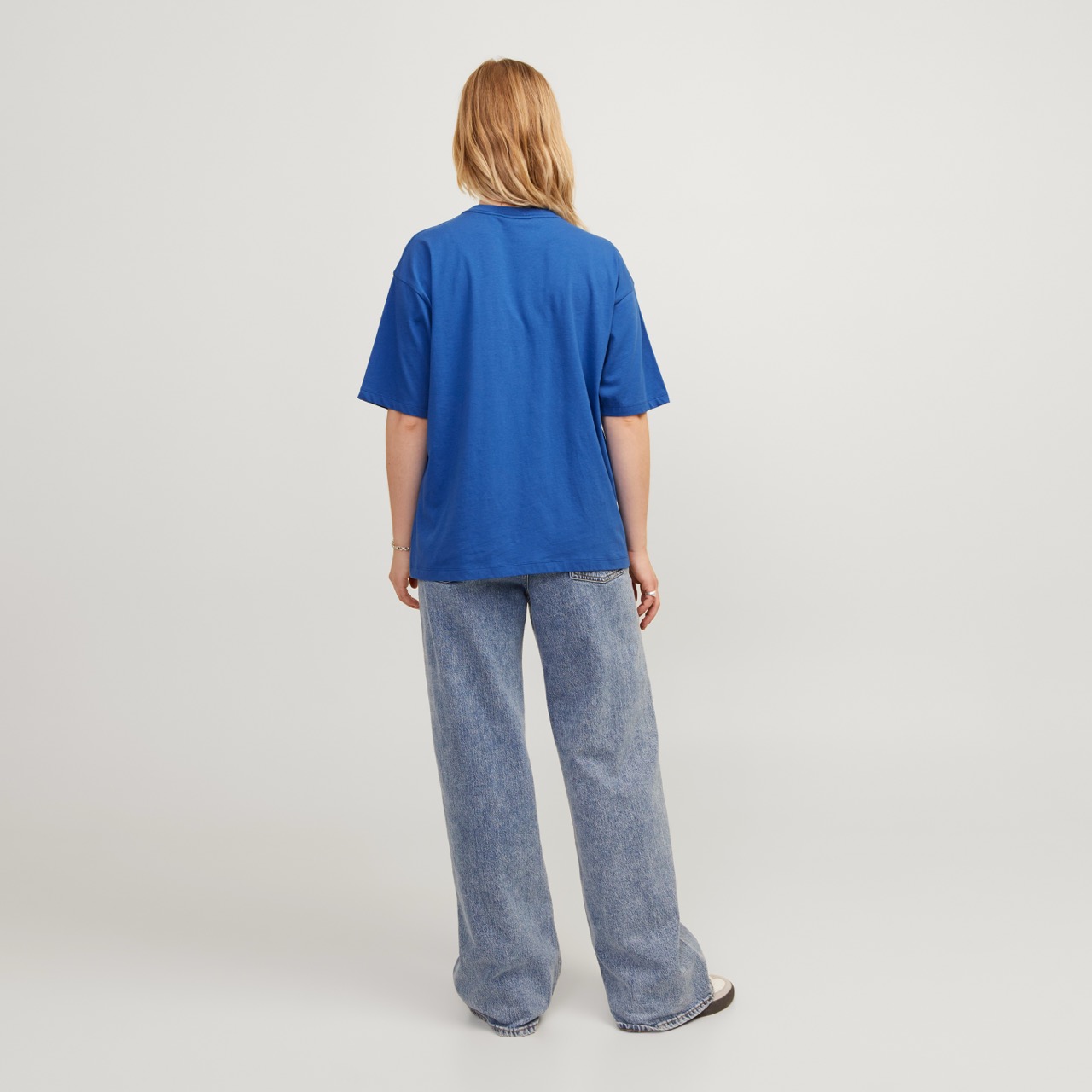 Mulher de costas com camisola azul e calças de ganga largas