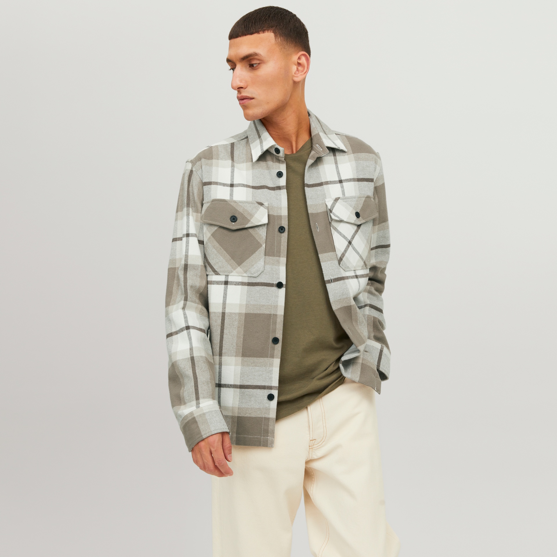 Homem veste camisa xadrez bege e verde, calças claras, fundo branco