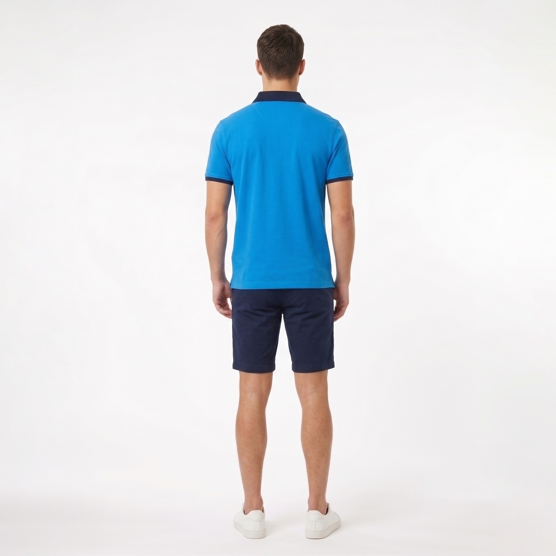 Homem de costas usando camisa polo azul, calções azul escuro e ténis brancos