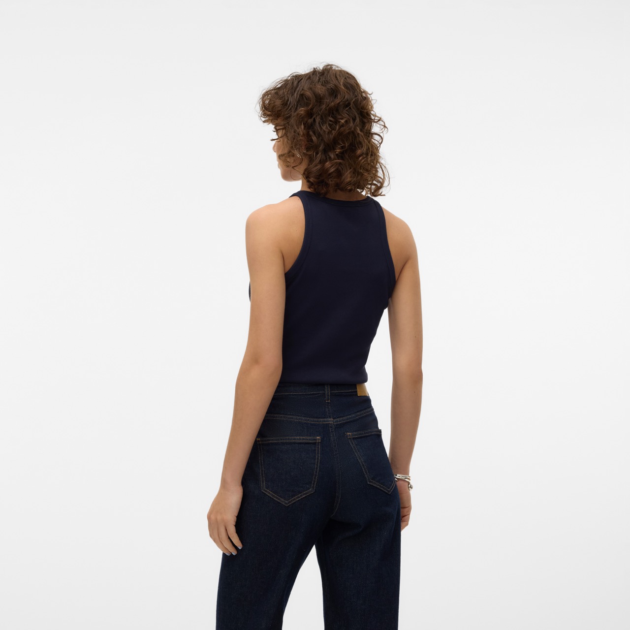 Mulher de costas com camisola preta sem mangas e calças de ganga azul escuro