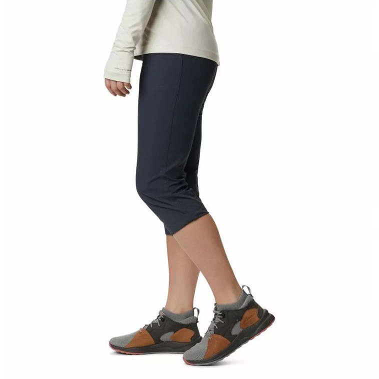 Pessoa de pé de lado usando calças capri azul-escuras e ténis cinza e castanhos