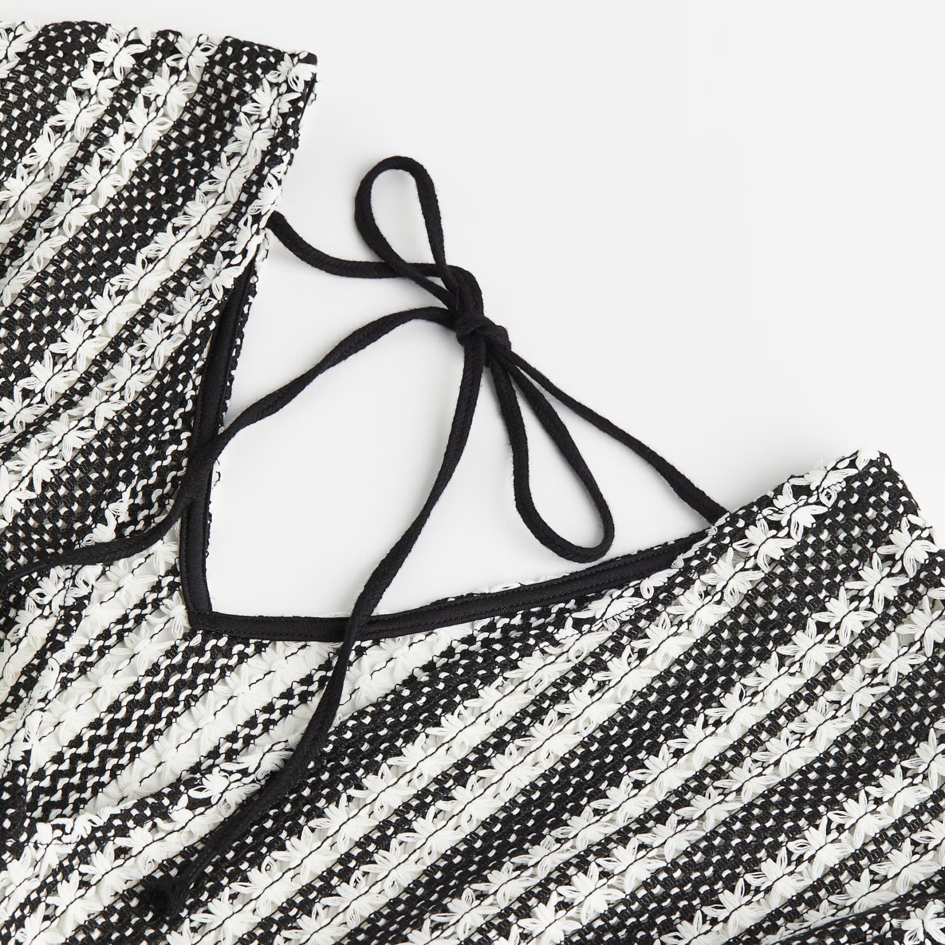 Parte superior de biquíni com padrão preto e branco de crochê com cordões pretos.