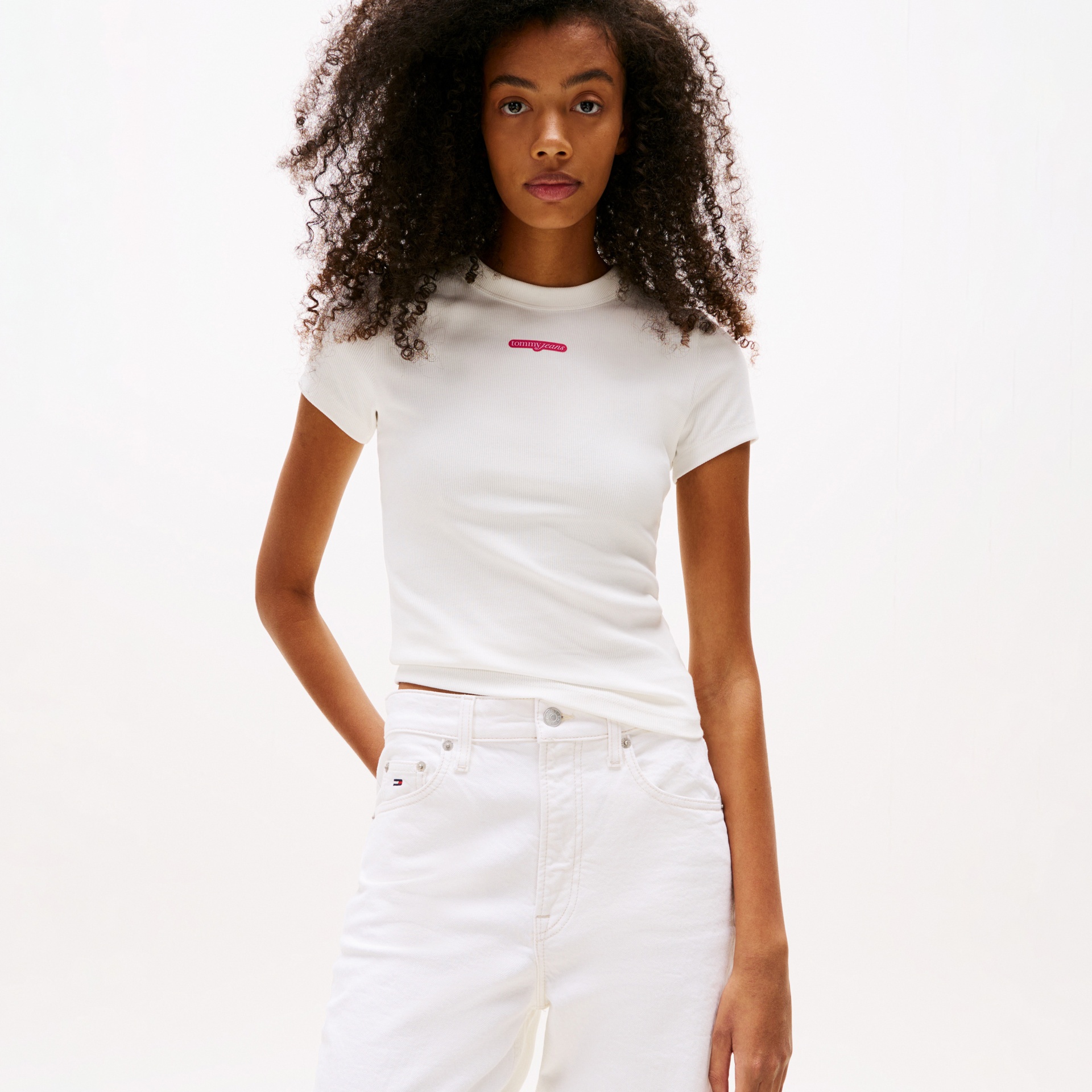 Mulher a usar t-shirt branca de manga curta com logo tommy jeans e calças brancas.