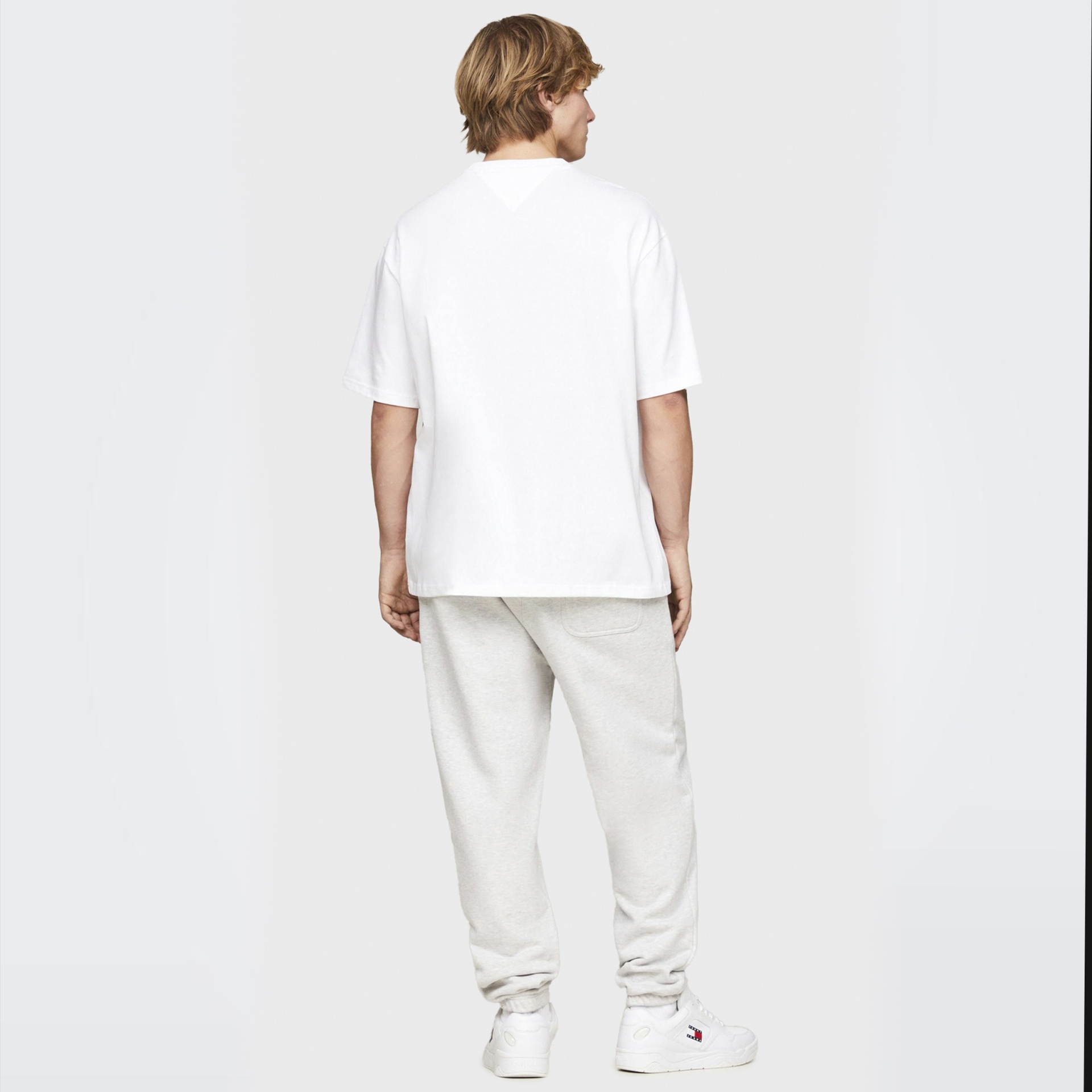 Homem de costas com t-shirt branca, calças cinza claro e sapatos brancos