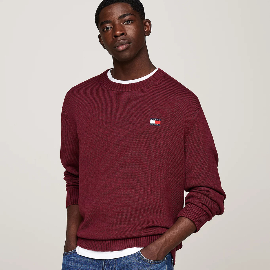 Camisola de malha grená com logótipo Tommy Hilfiger, usada por homem com t-shirt branca por baixo e jeans azuis