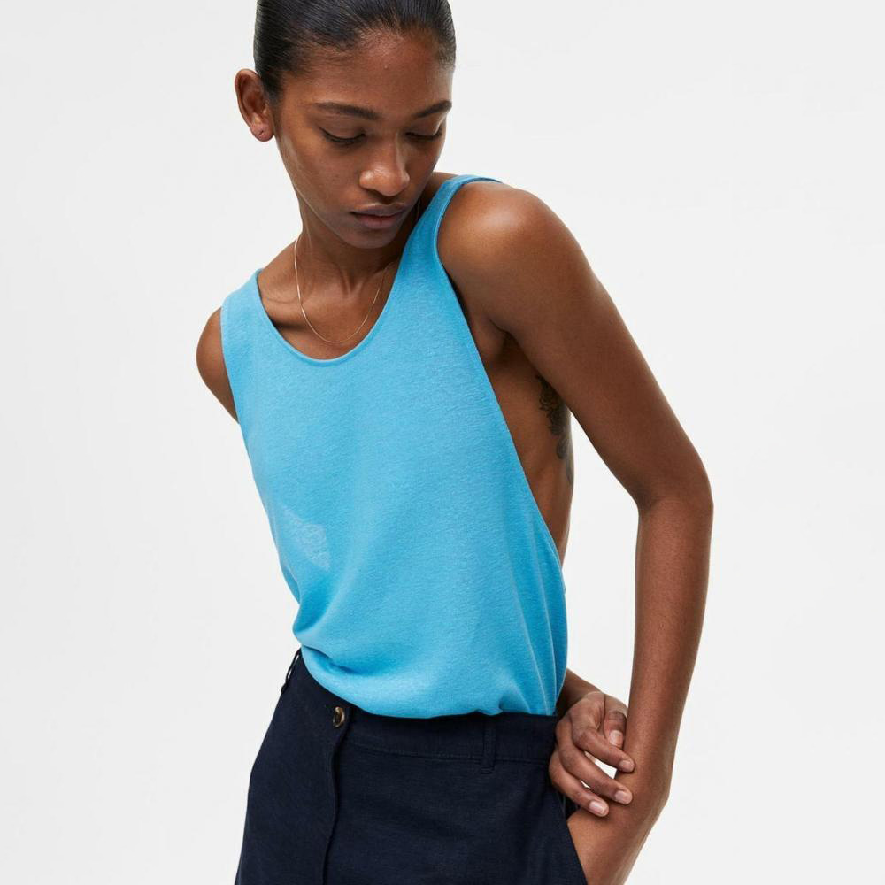 Mulher veste camisola azul sem mangas e calças escuras em fundo branco