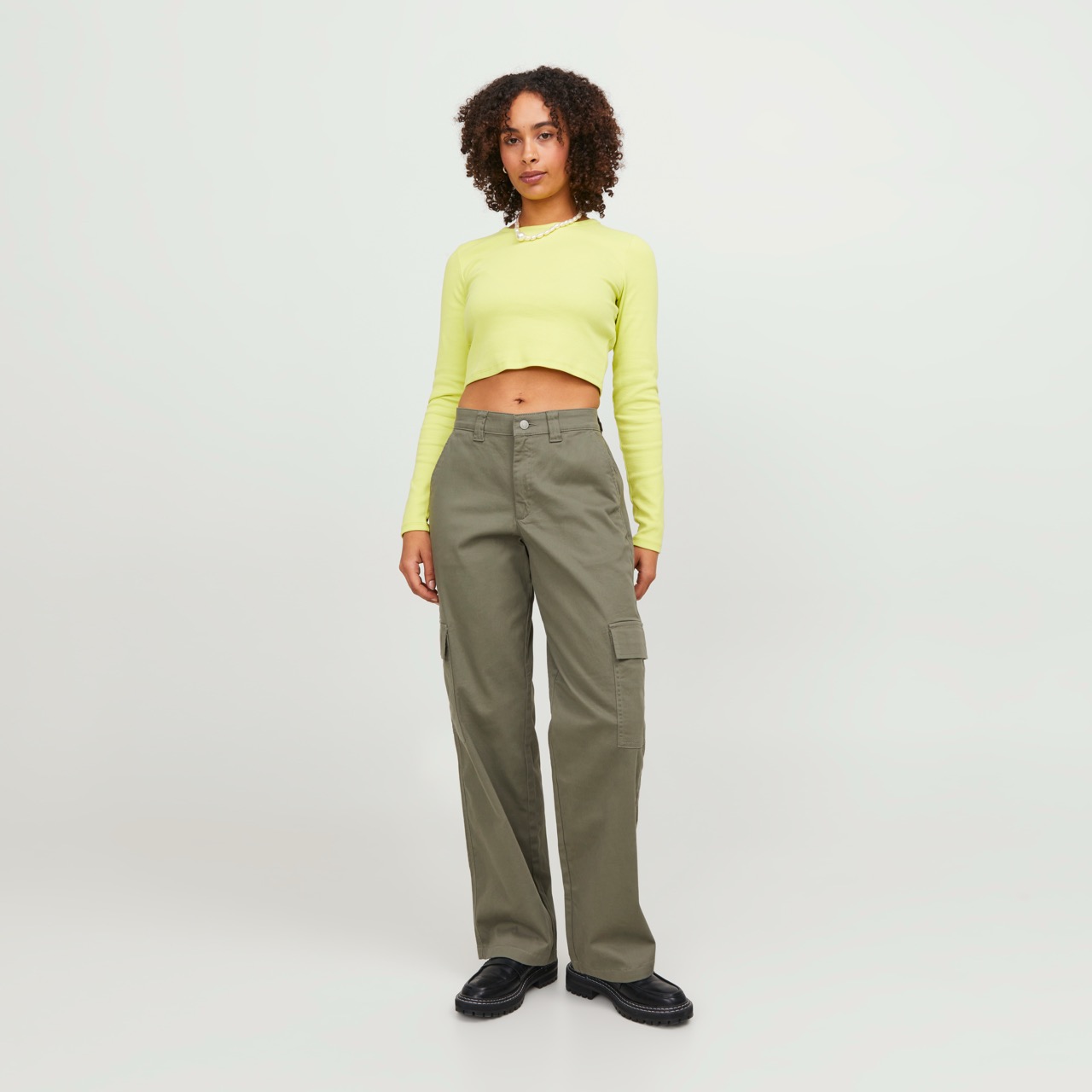 Mulher com top amarelo claro e calças cargo verde-oliva num fundo branco