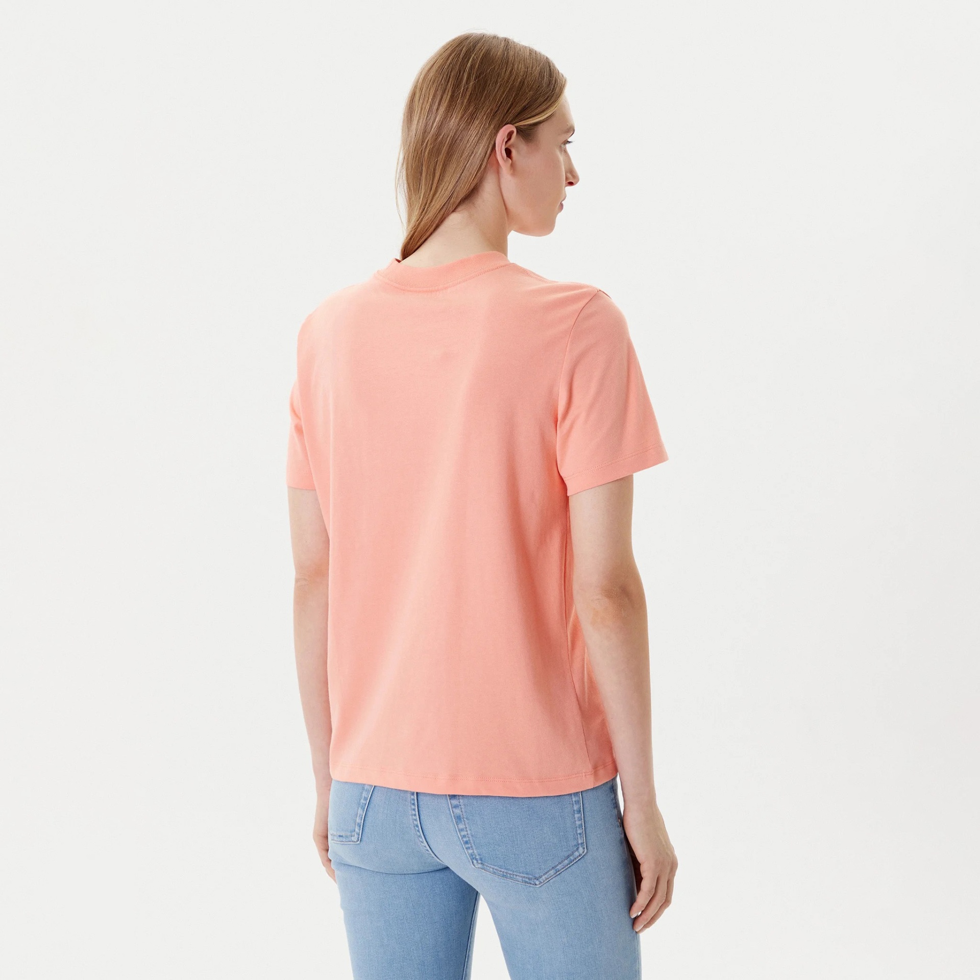 T-shirt feminina salmão vista de costas com jeans azul claro em fundo branco.