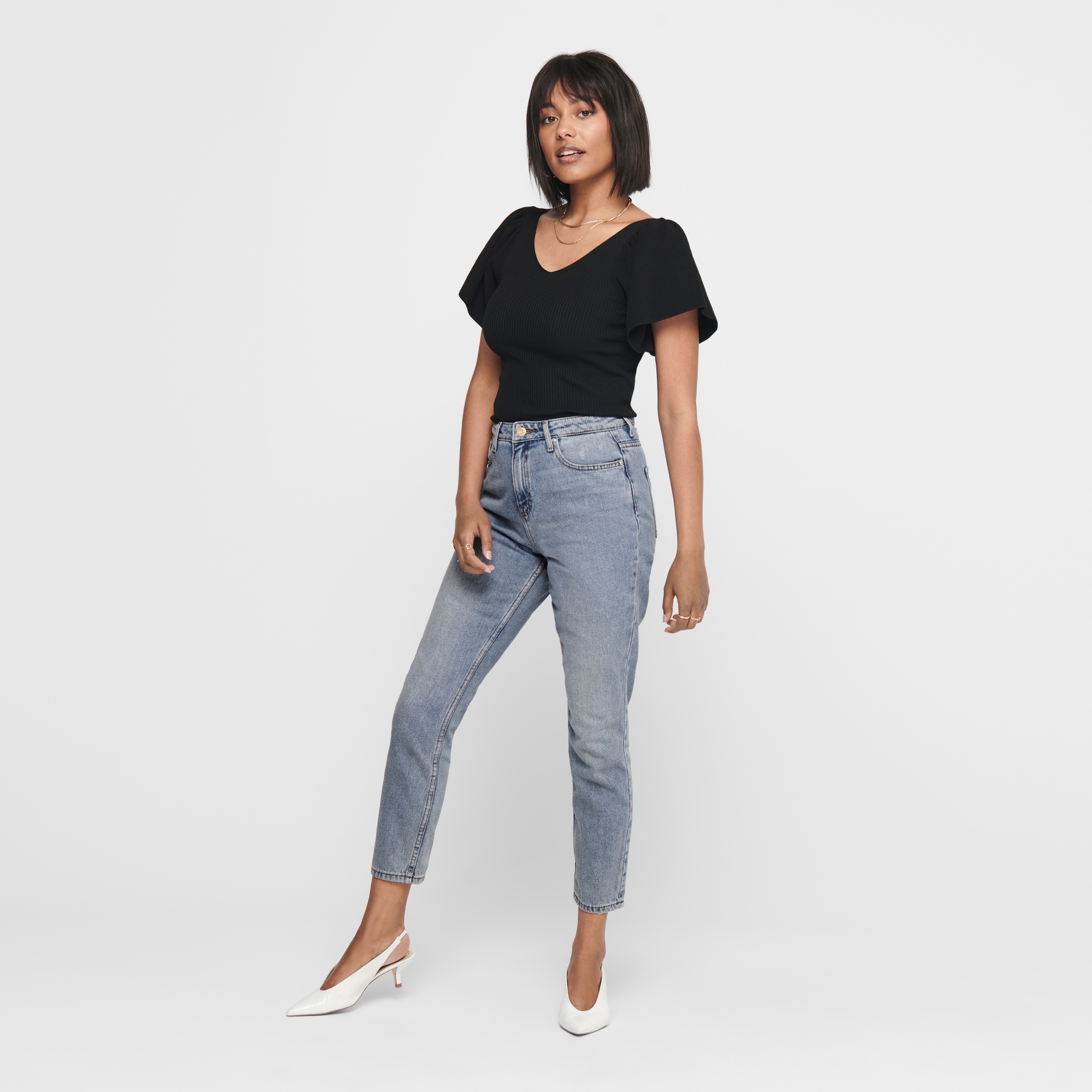 Mulher vestindo camisa preta de manga curta e calças de ganga azul claro com sapatos brancos.