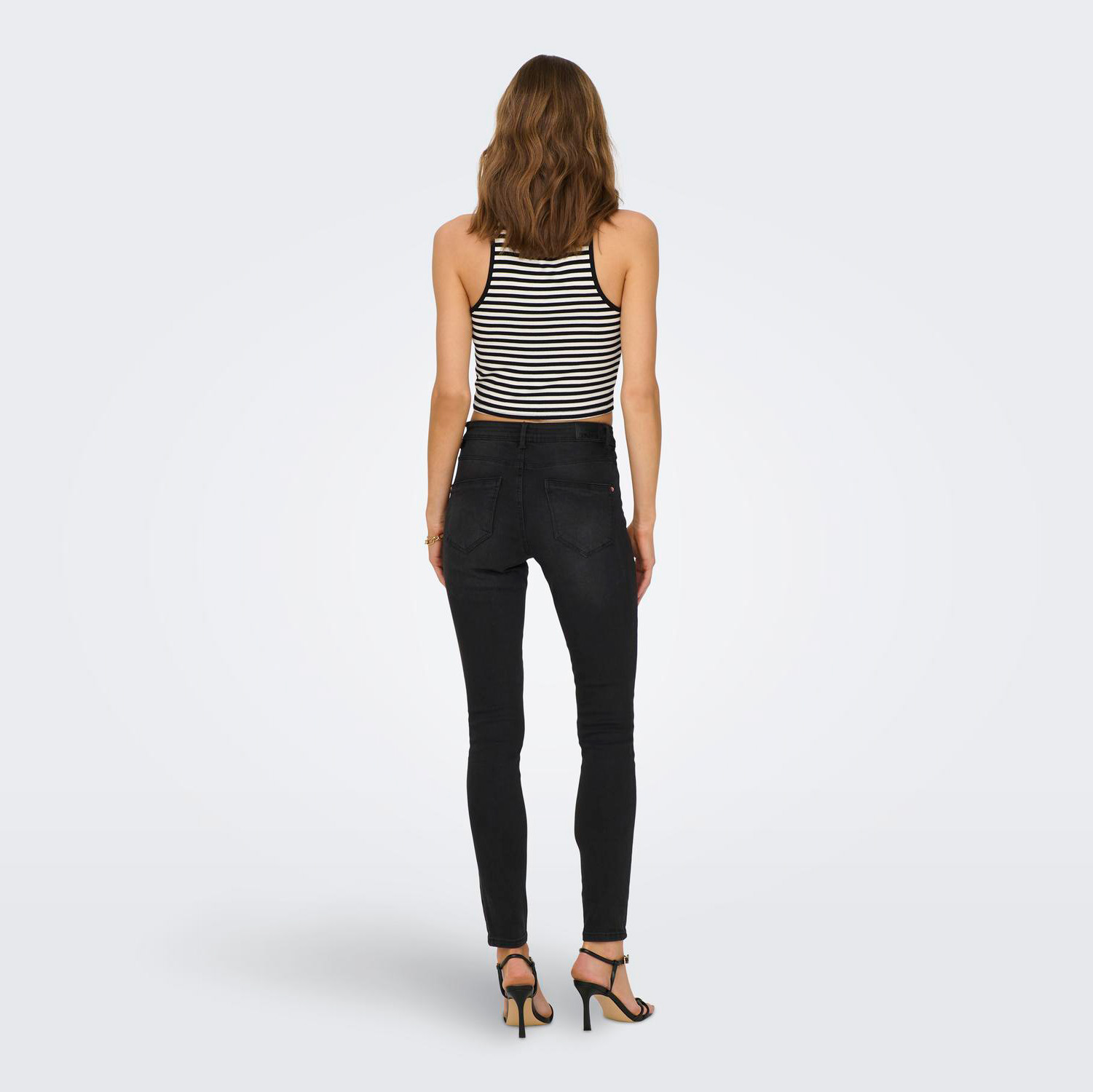 Mulher de costas com calças pretas skinny e top riscas