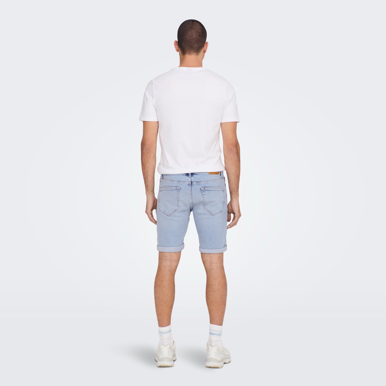 Homem de costas com t-shirt branca, calções azuis e ténis brancos