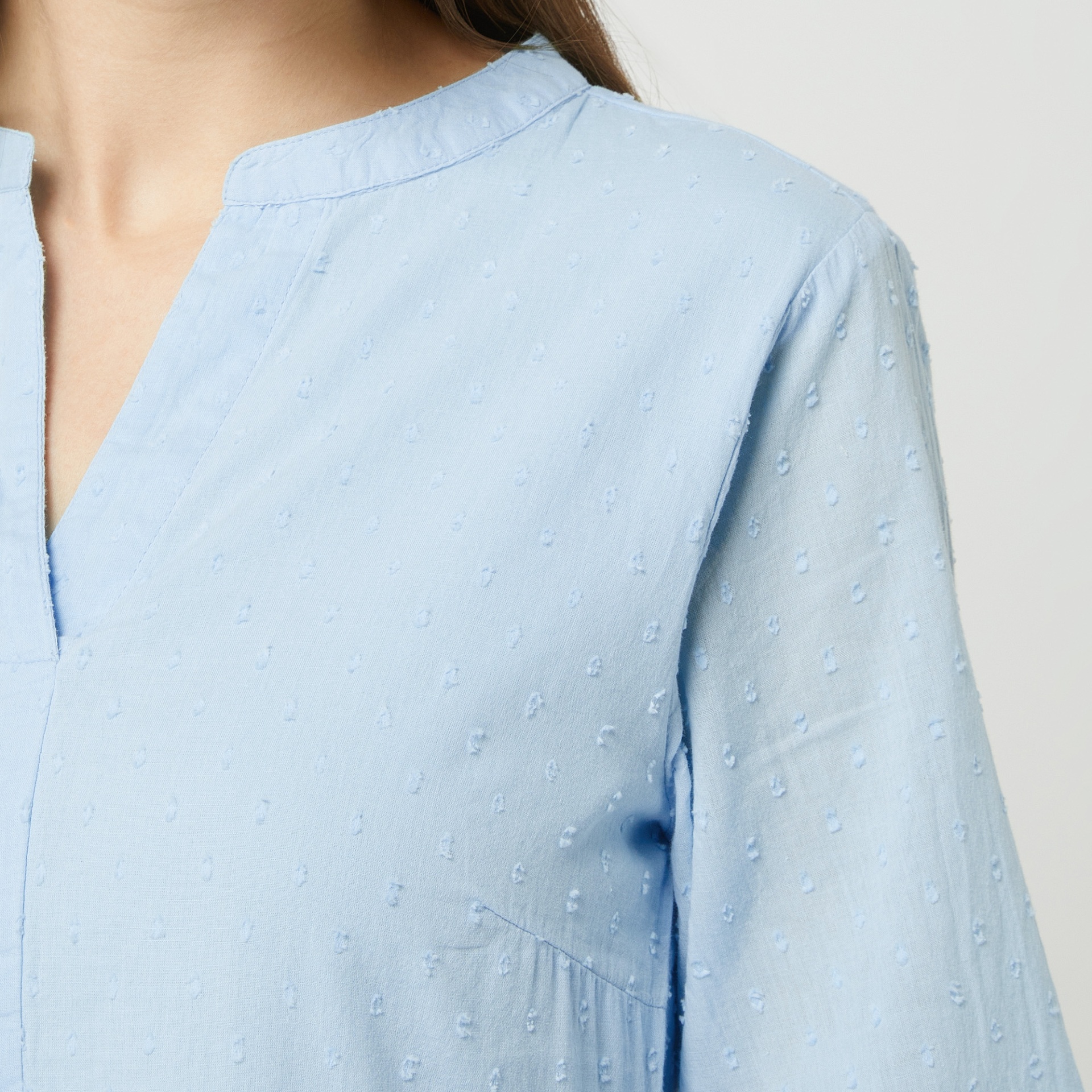 Blusa azul clara de tecido leve com textura plumeti e gola redonda com abertura em V