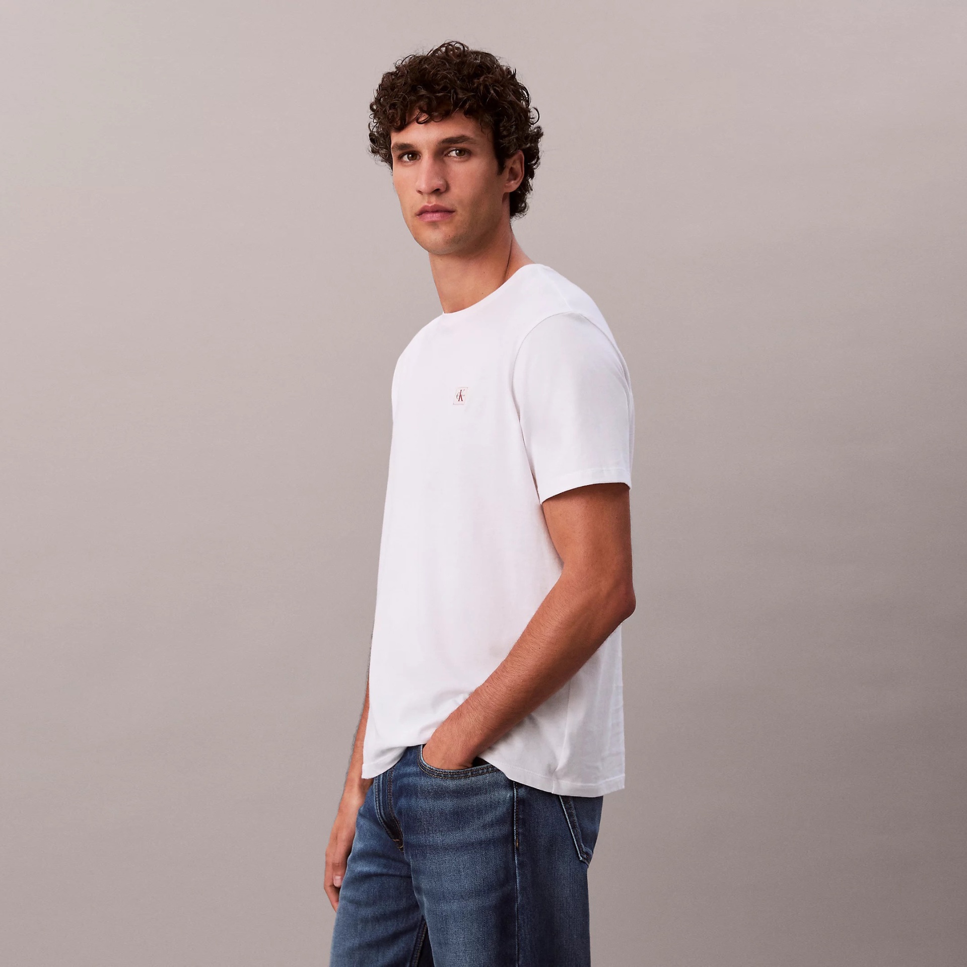 Camisola branca com logótipo CK rosa usada por modelo com calças de ganga azuis