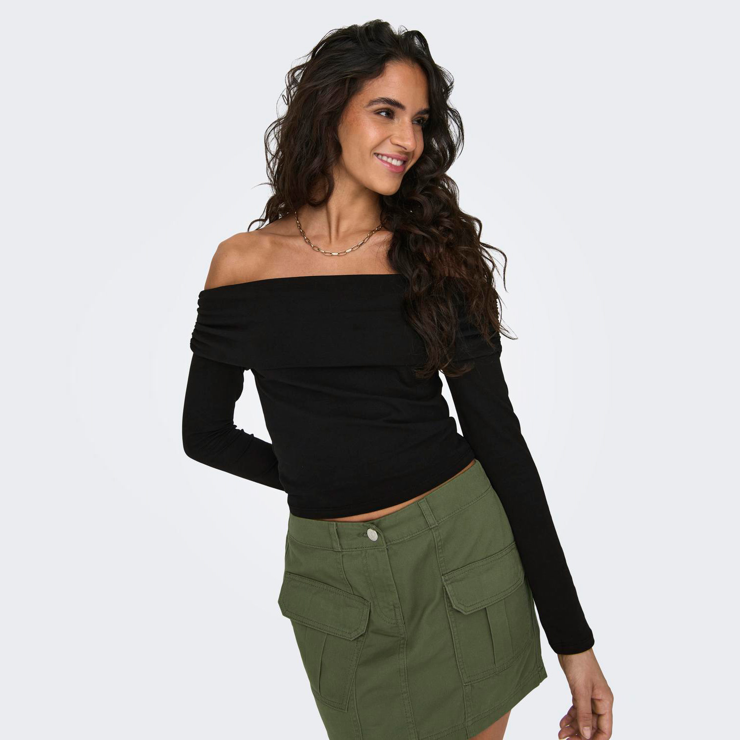 Mulher com blusa preta ombro a ombro e saia verde posando