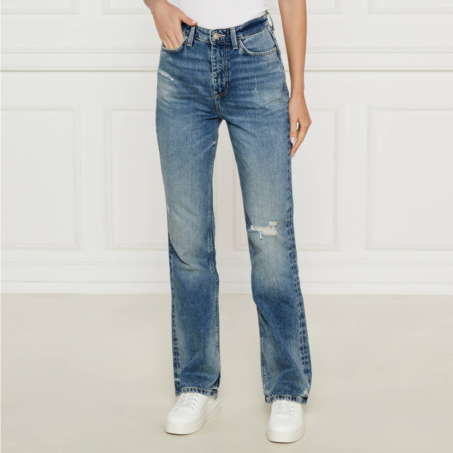 Calças de ganga azuis com rasgos e efeito desgastado usadas com top branco e sapatos brancos