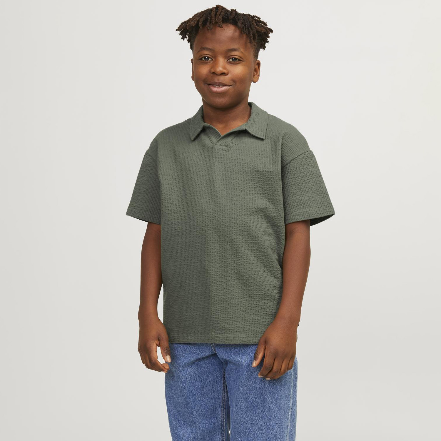 Menino com t-shirt verde escura de manga curta e calças de ganga azul claro