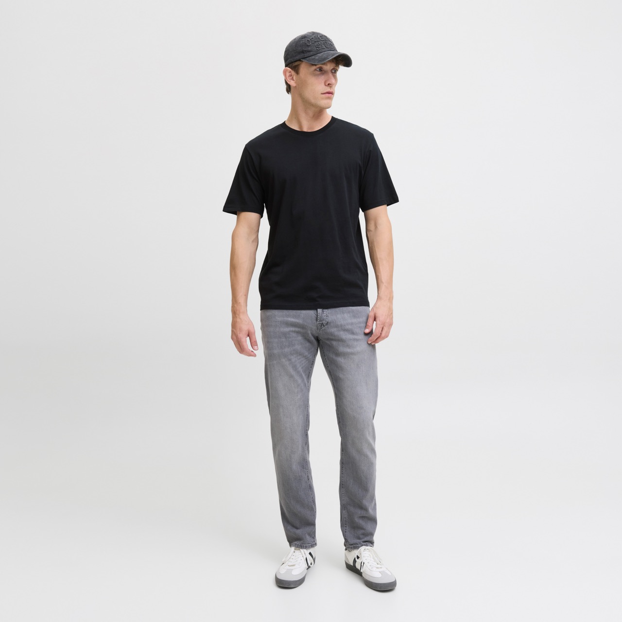 Homem com t-shirt preta, calças cinza, boné preto e ténis brancos