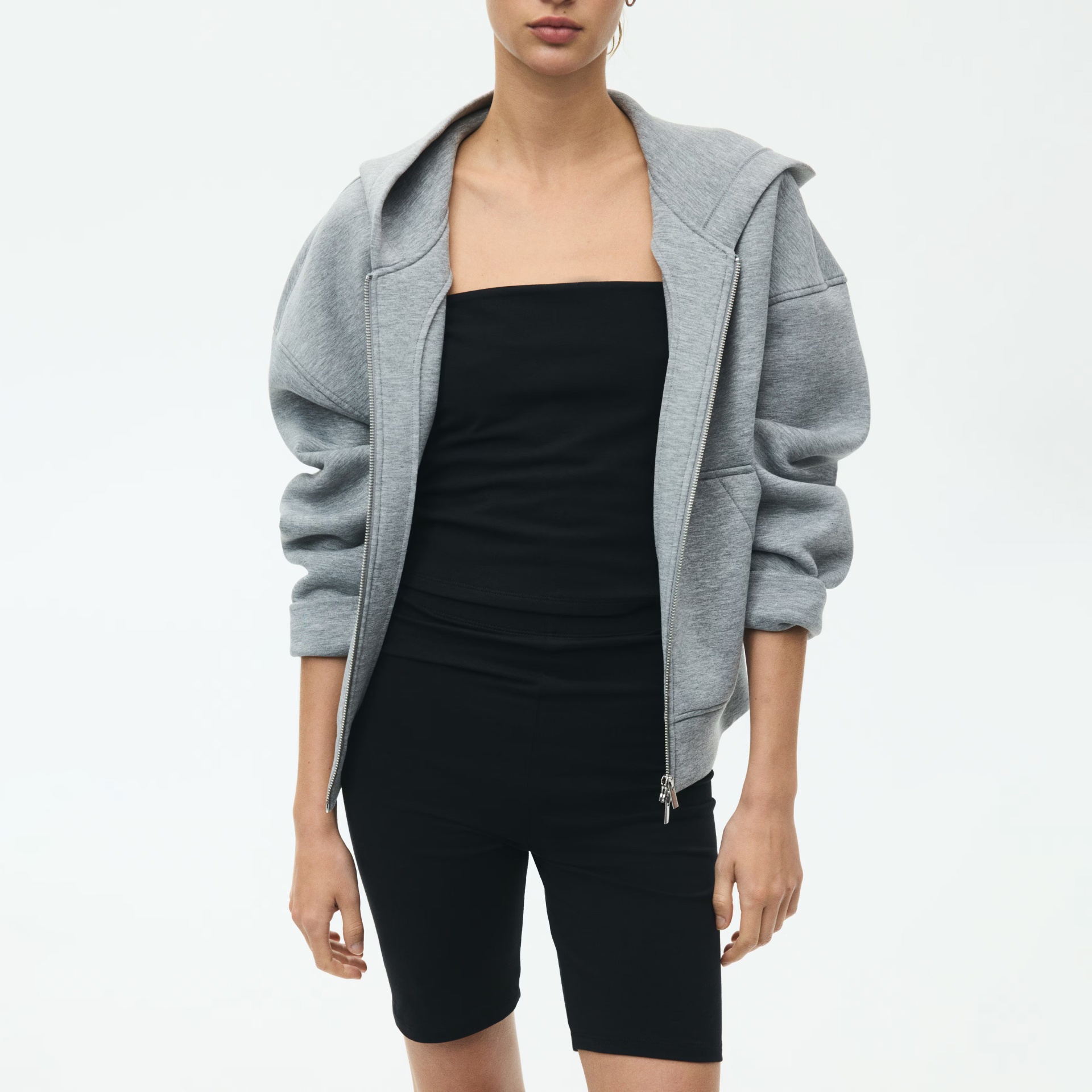 Pessoa vestindo camisola cinzenta com capuz, top preto e calções pretos