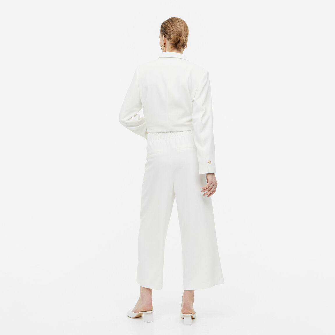 Calças e blazer brancos femininos vistos de costas em fundo branco