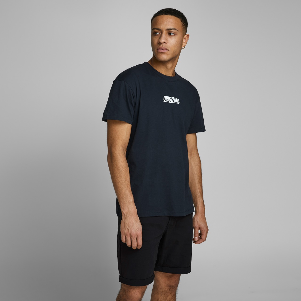 Modelo veste t-shirt preta com texto 'ORIGINALS' e calções pretos