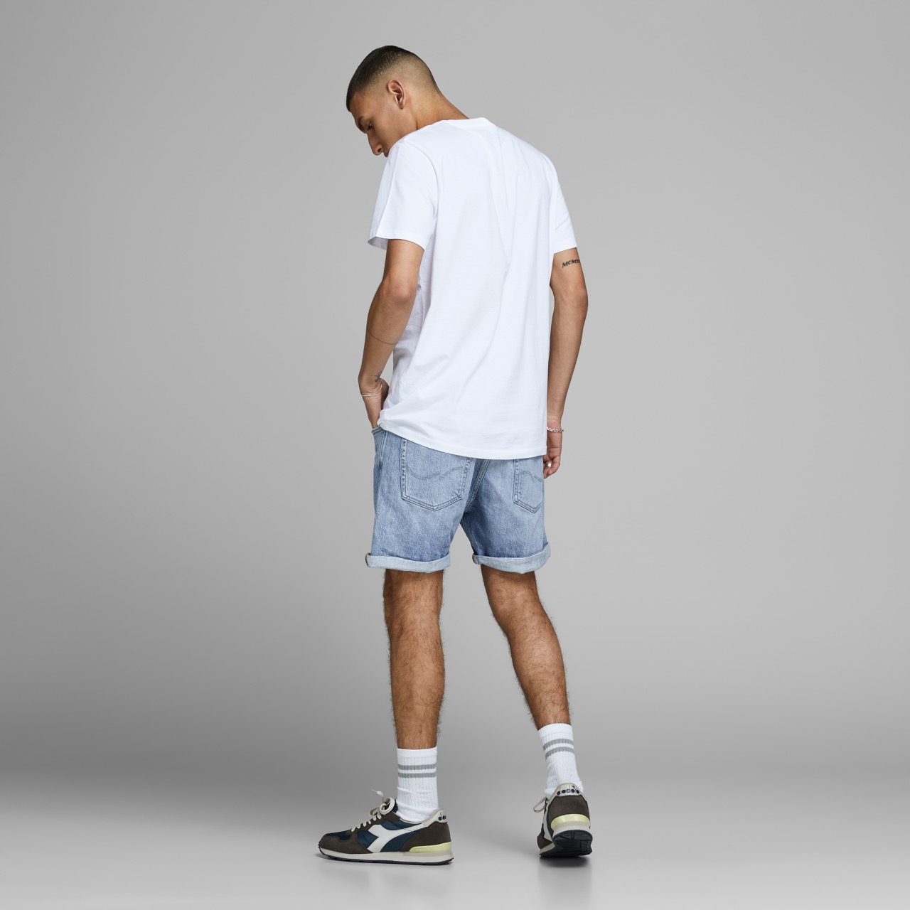 Homem de costas a vestir camiseta branca, calções de ganga e ténis