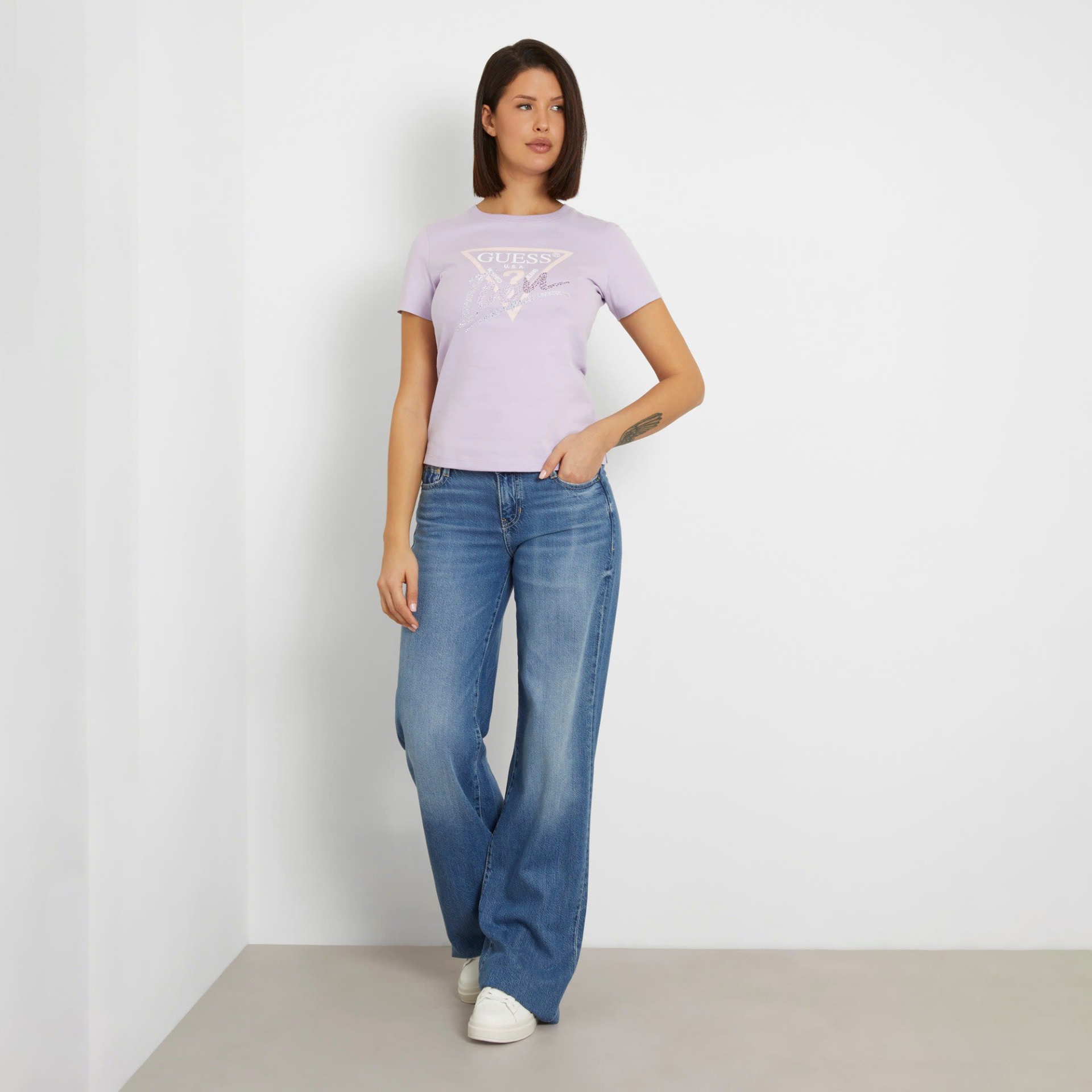 Mulher a usar t-shirt lilás com logo e calças de ganga azuis largas