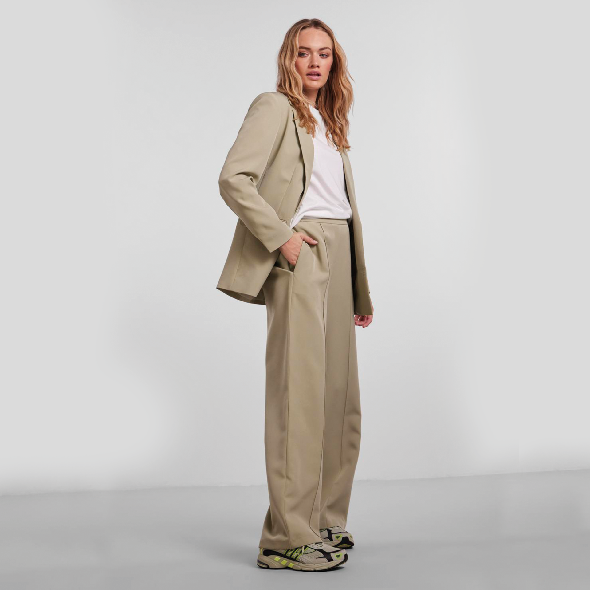 Mulher vestindo conjunto bege de blazer e calças largas com t-shirt branca e sapatilhas multicoloridas