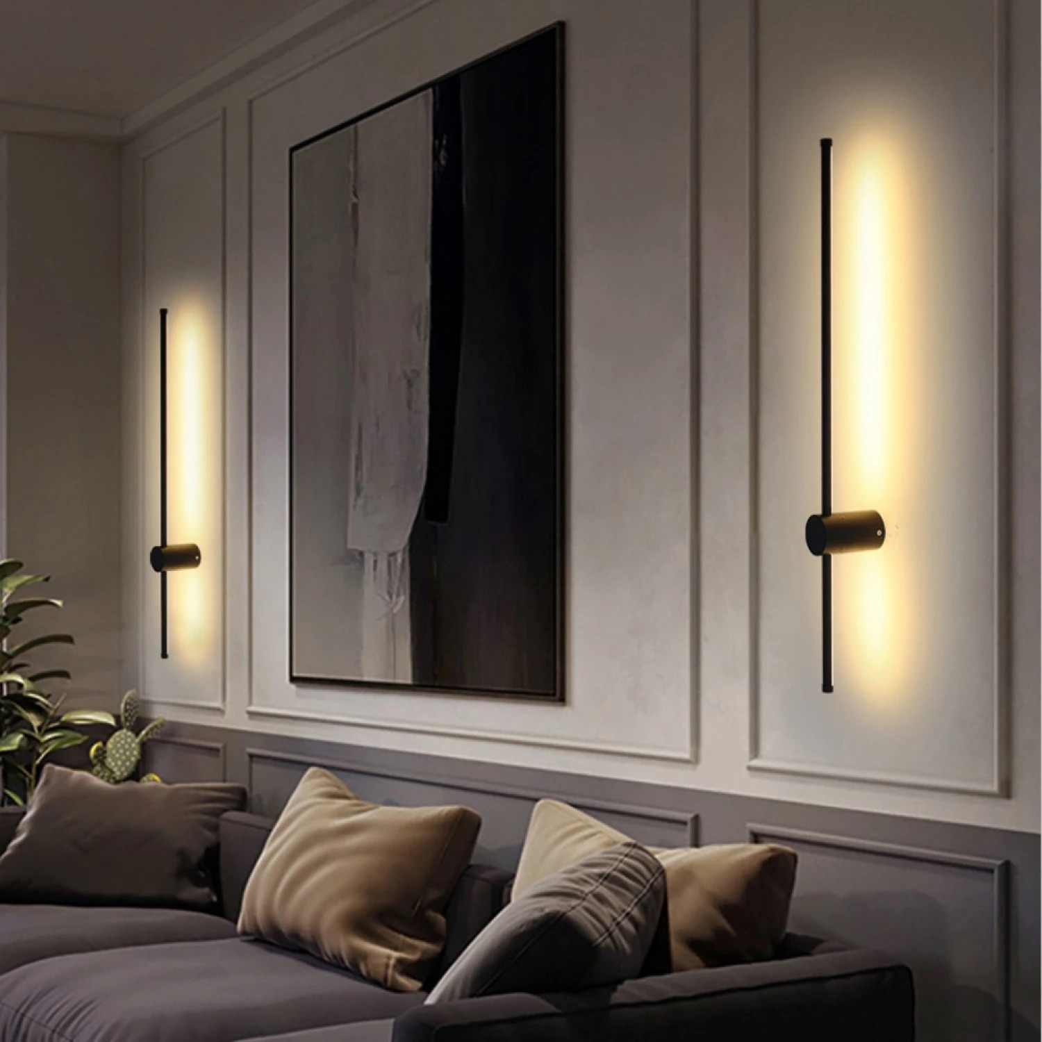 Arandelas verticais pretas com luz amarela numa parede azul clara com molduras, sofá com almofadas coloridas e plantas, quadro abstrato na parede