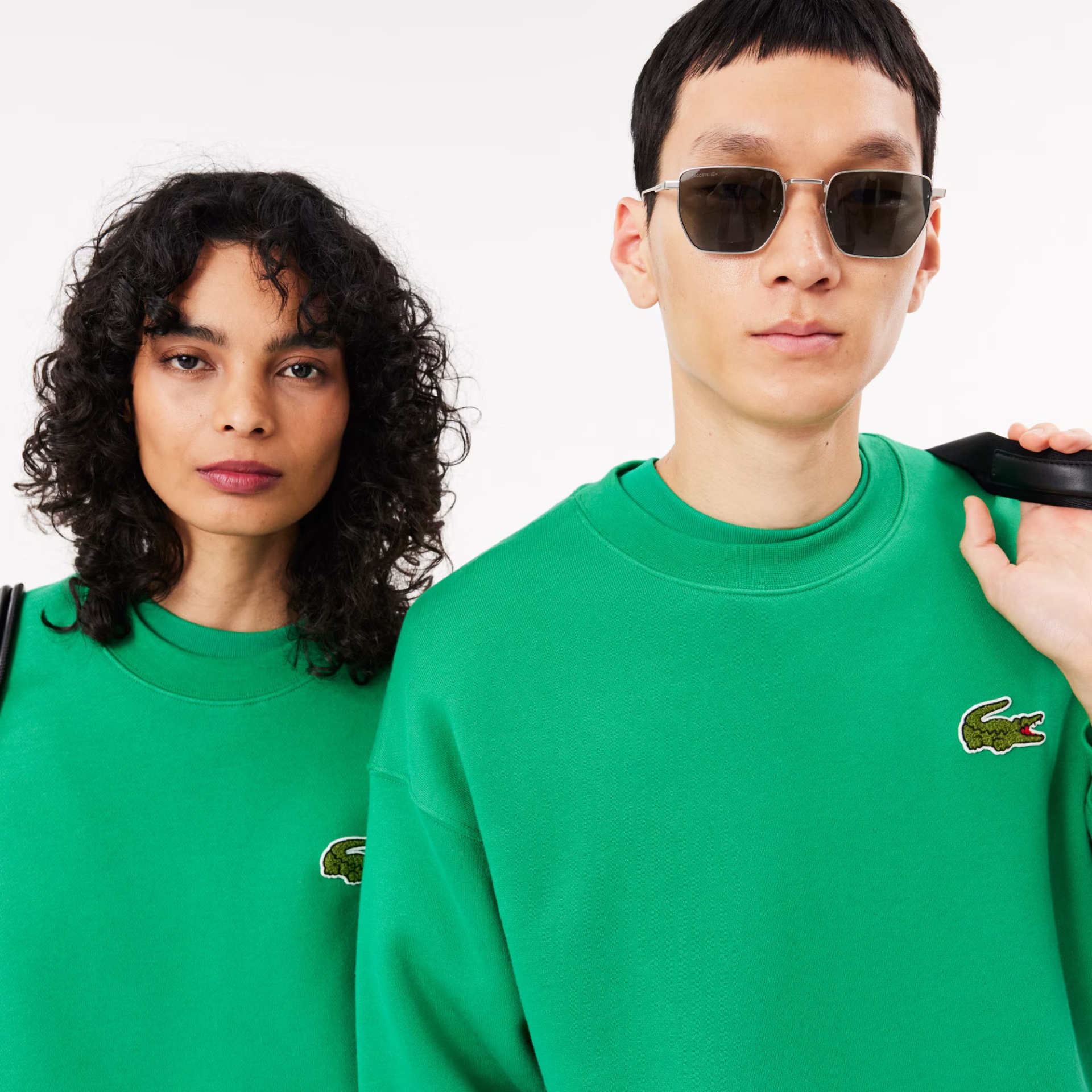 Duas pessoas com sweatshirts verdes com logótipo de crocodilo e óculos de sol.
