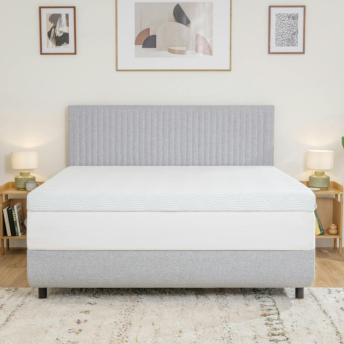 Cama cinza com colchão branco e decoração de quarto com quadros e candeeiros.
