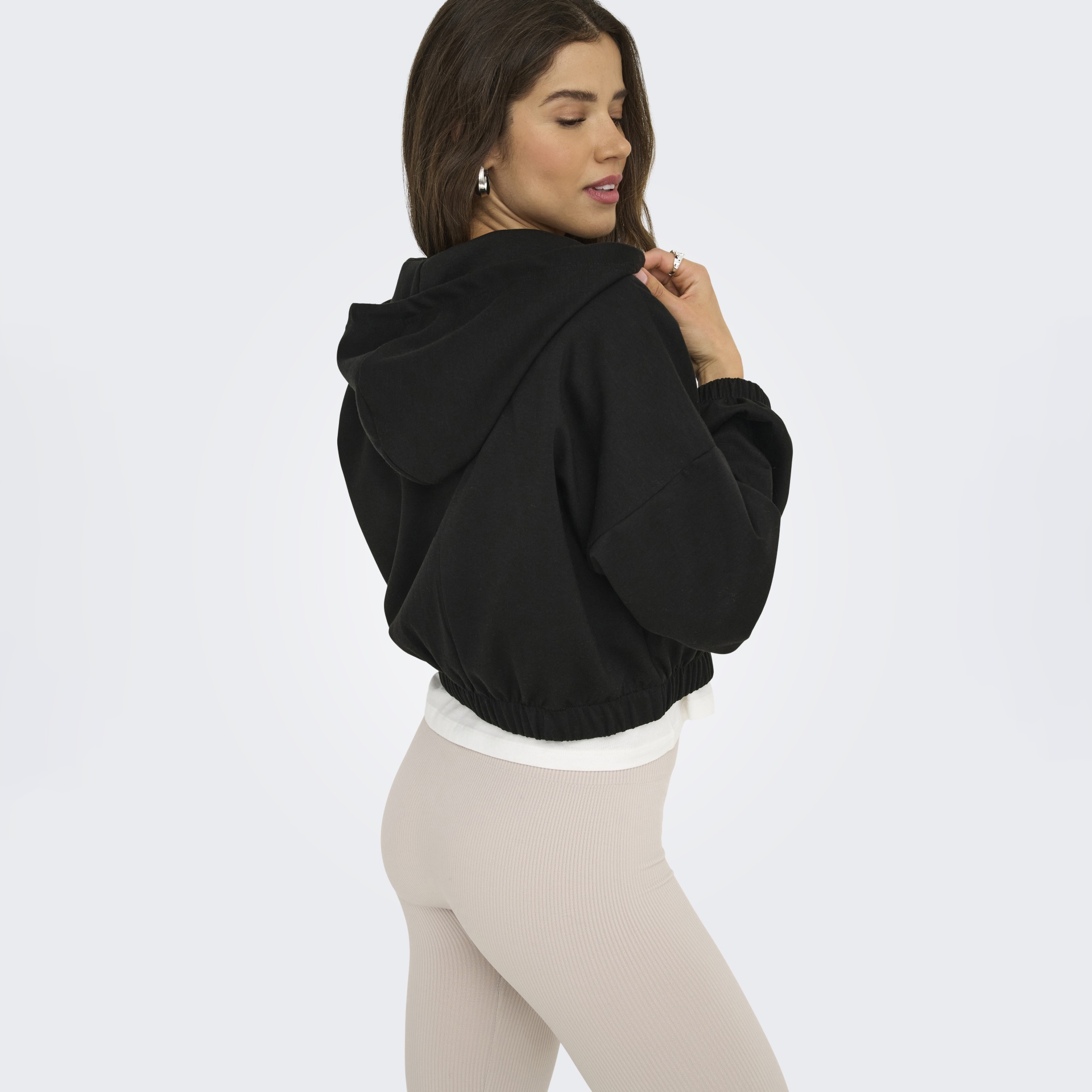Mulher de perfil com hoodie preto e calças bege justas