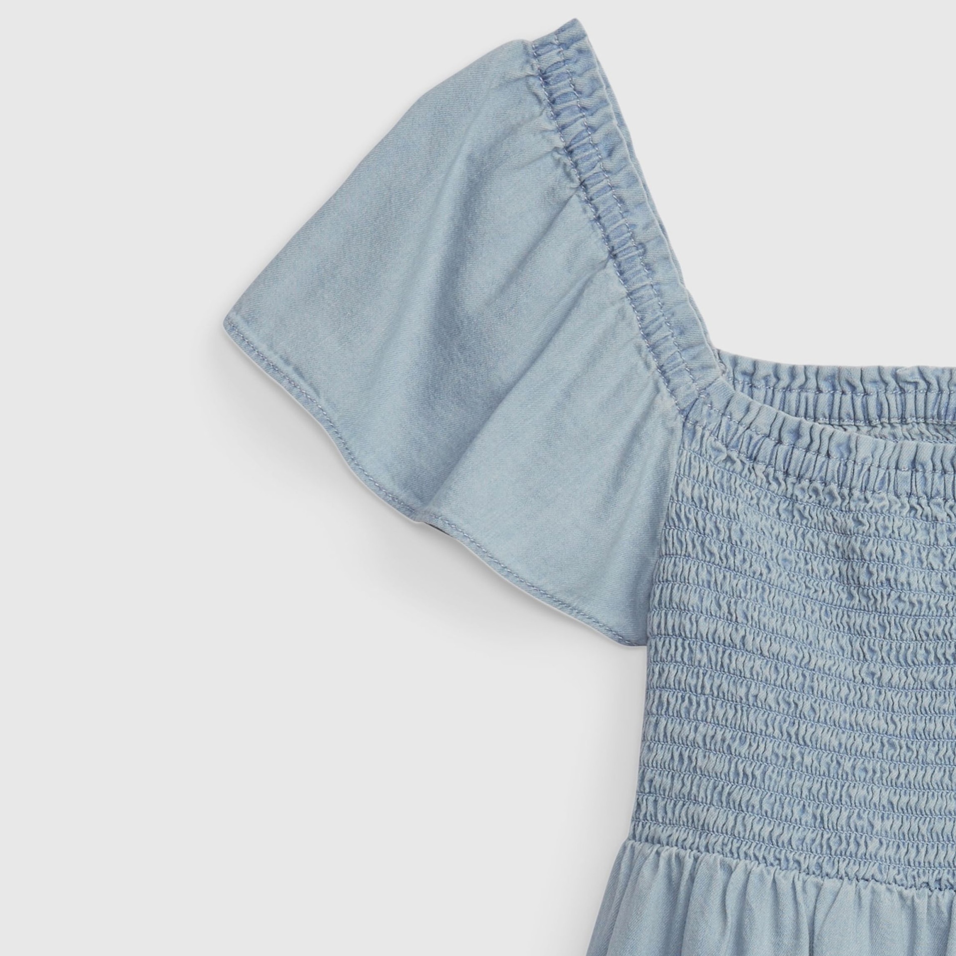 Detalhe de parte superior de vestuário azul claro em tecido denim com mangas curtas e franzido.