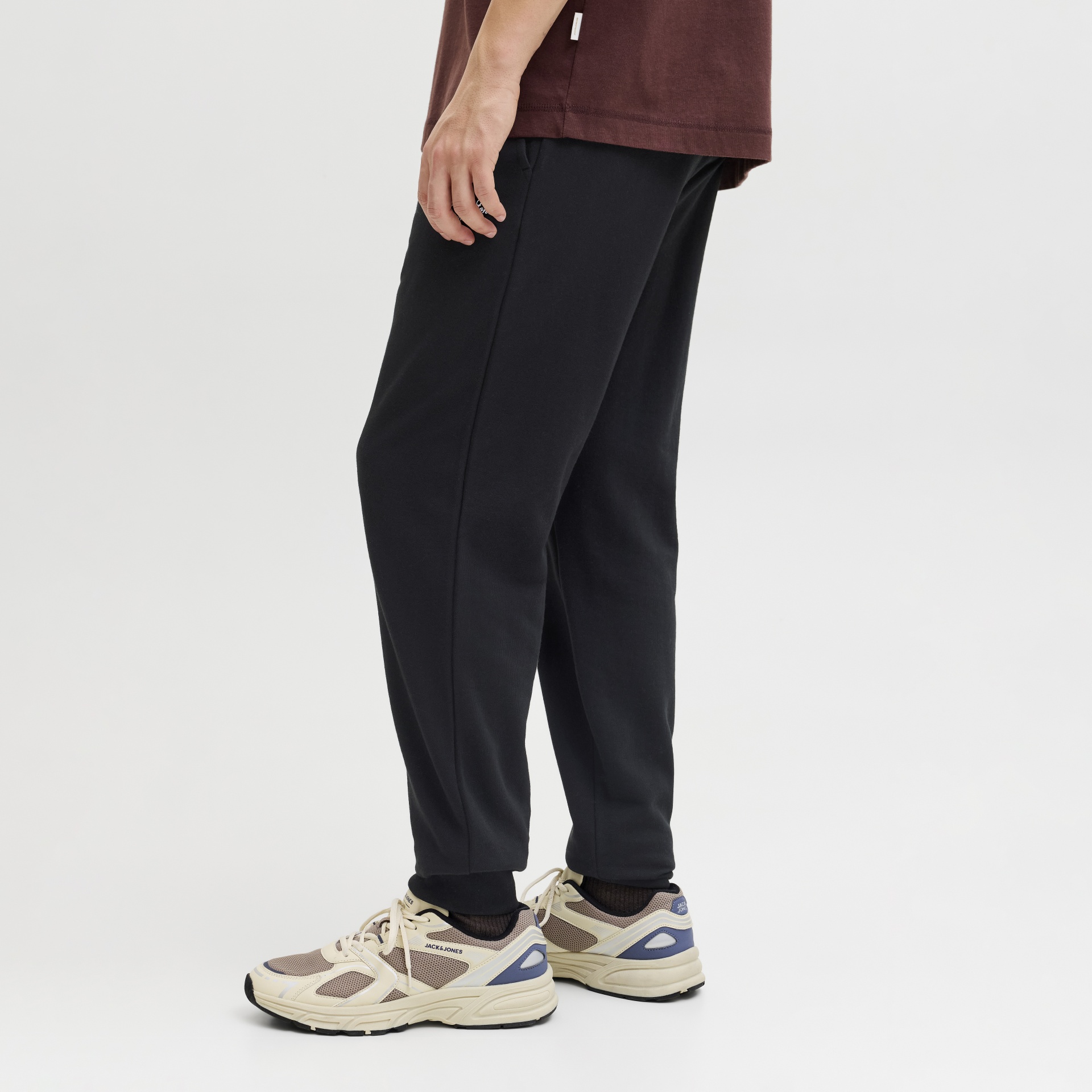 Calças pretas com ténis Jack & Jones bege e azul, fundo branco.
