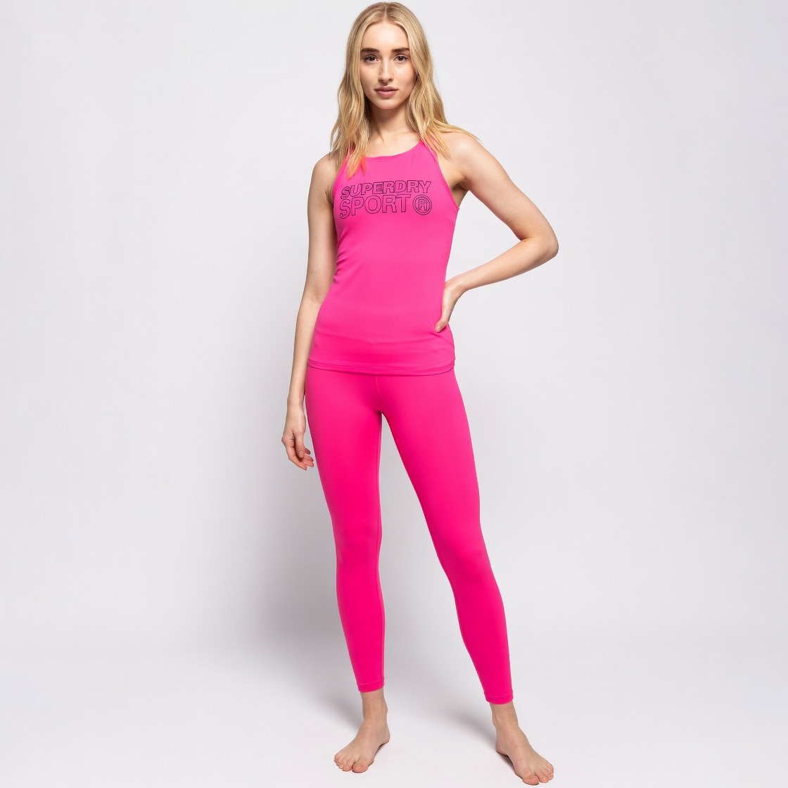 Conjunto desportivo rosa fluorescente com camisola de alças e leggings, mulher em fundo branco.