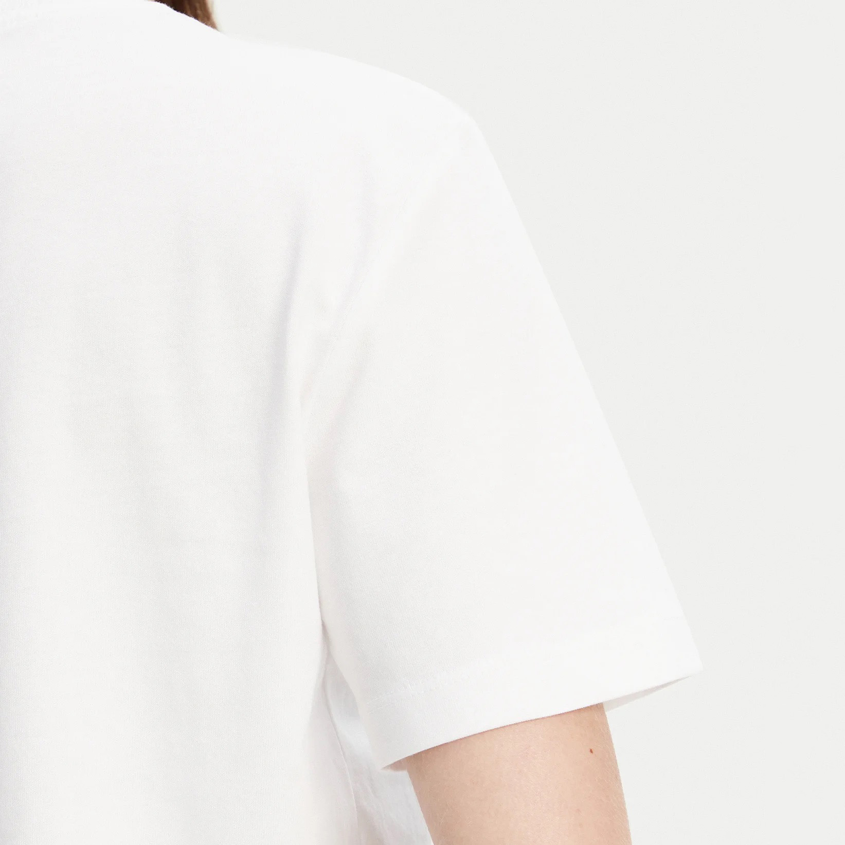 T-shirt branca de manga curta em tecido liso vista de perto no ombro e braço.