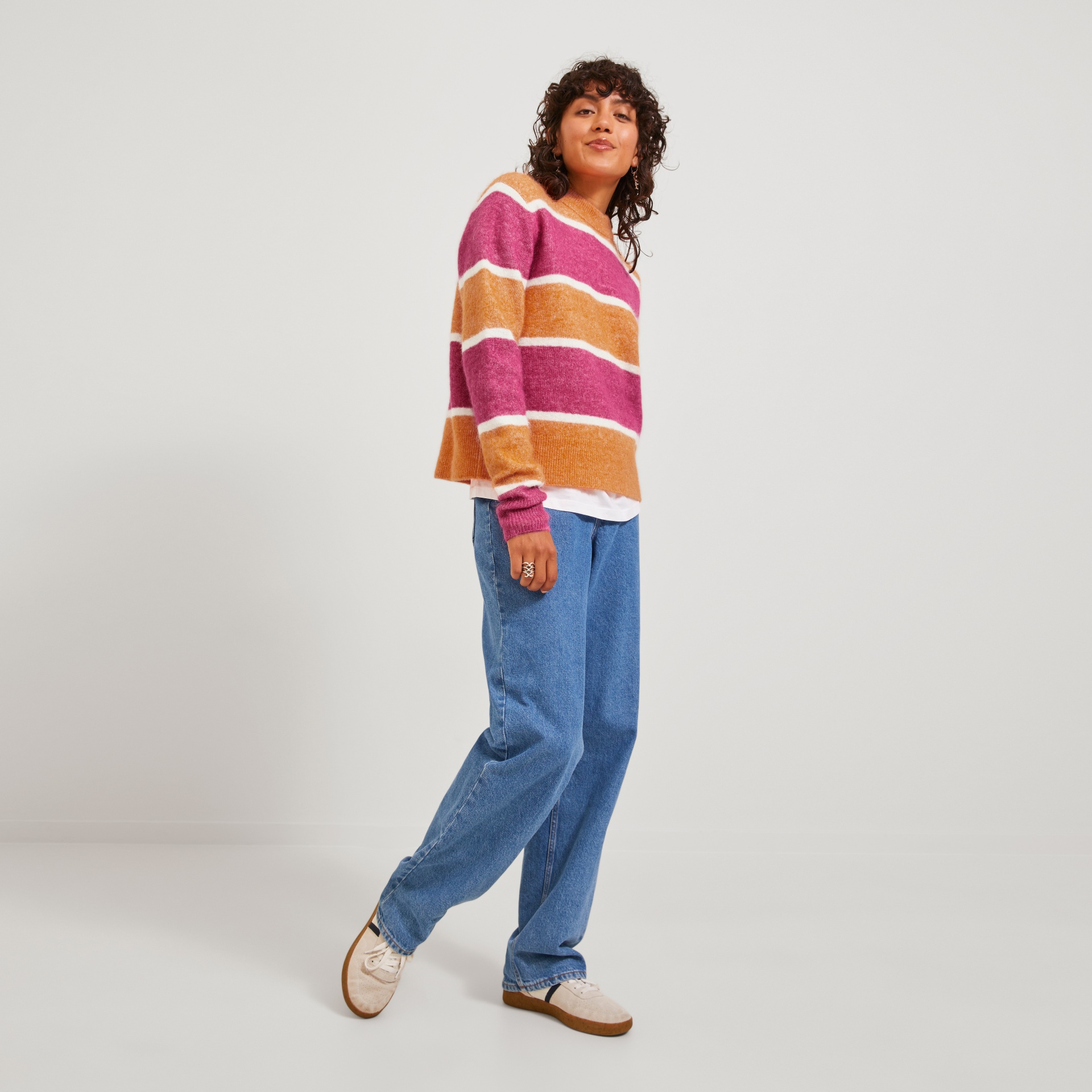 Mulher com camisola riscada rosa e laranja, jeans azul largos e ténis brancos
