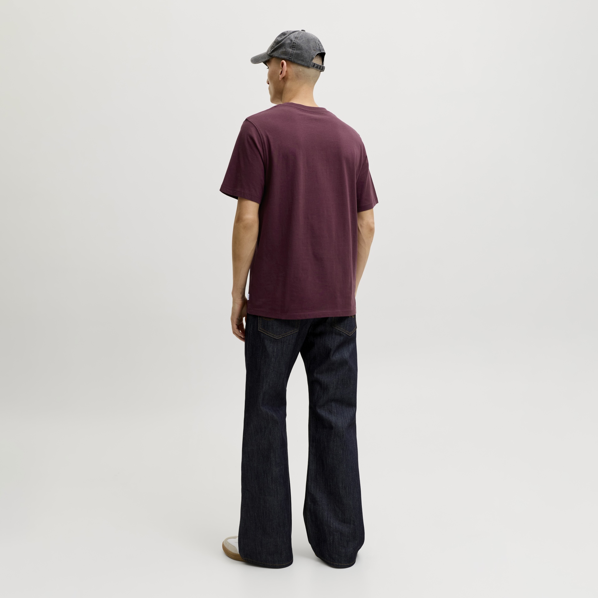 Homem de costas com t-shirt vinho, calças de ganga largas e boné cinzento.