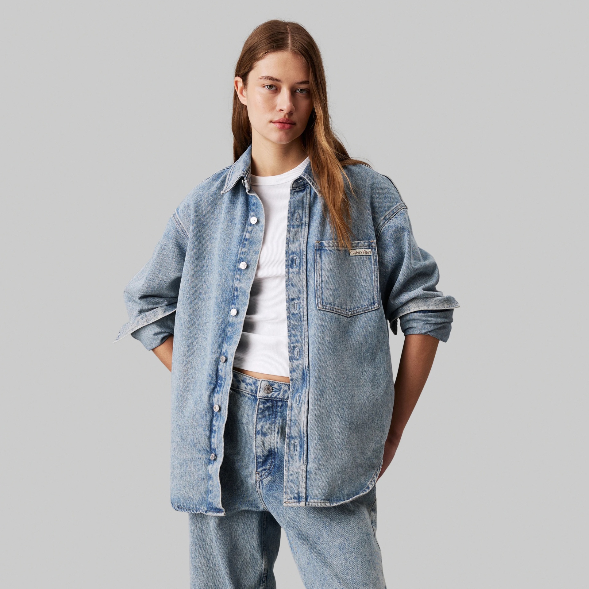 Mulher com camisa e calças de ganga azul claro, camisa com bolso e etiqueta Calvin Klein.