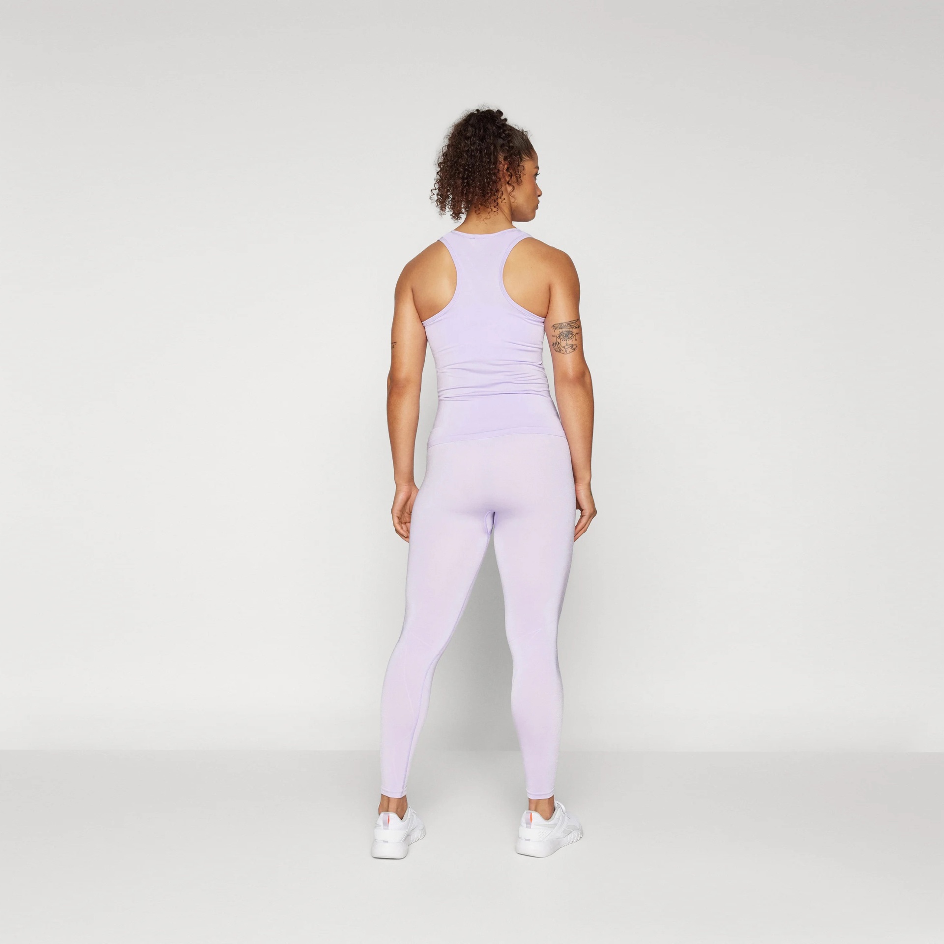 Mulher de costas a usar conjunto desportivo lilás com top e leggings