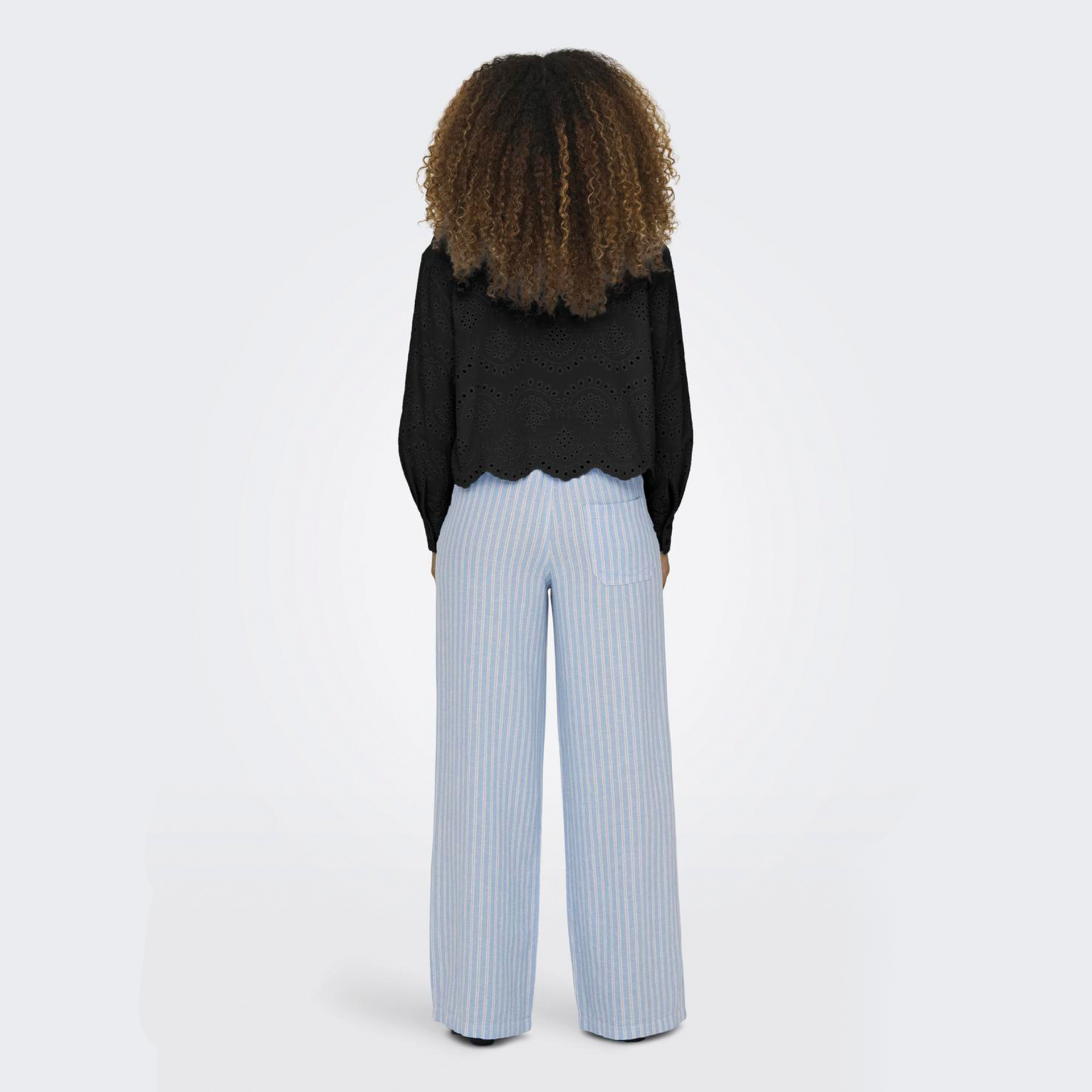 Pessoa de costas com calças riscadas azuis e brancas e blusa preta de manga comprida