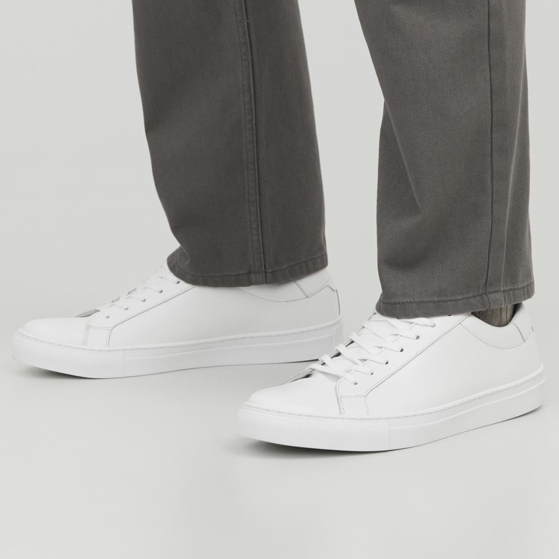 Sapatilhas brancas de couro com atacadores brancos usadas com calças cinza