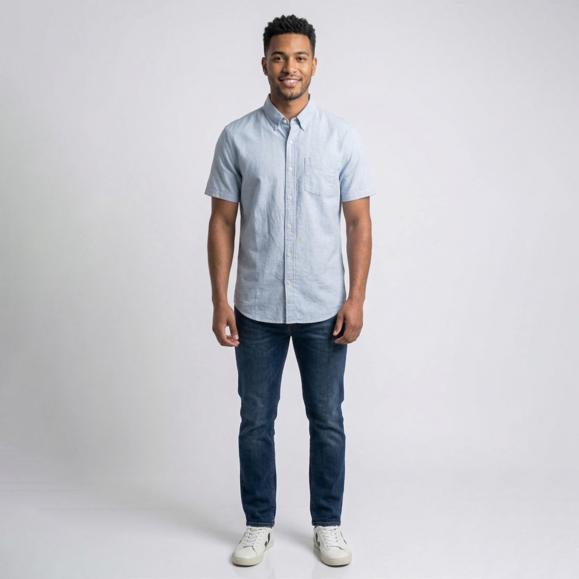 Homem com camisa azul clara de manga curta, jeans azul escuro e ténis brancos