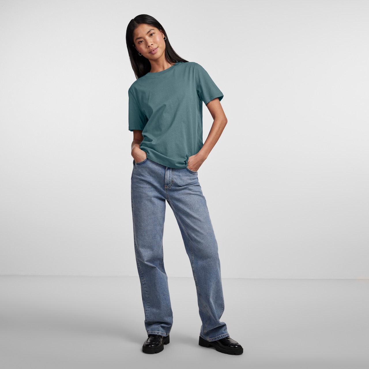 Mulher com t-shirt verde-azulada e jeans azuis posando