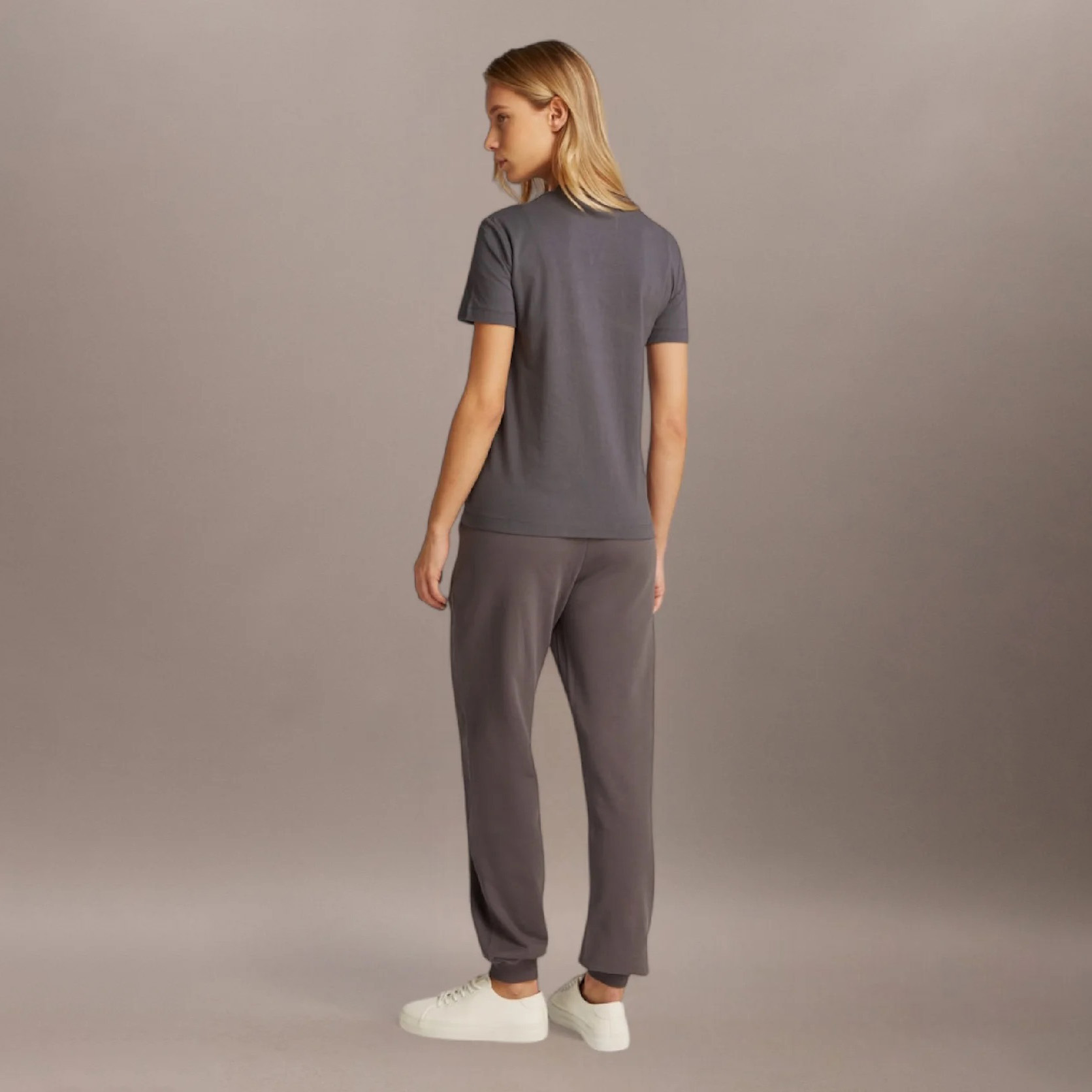 Pessoa de costas com t-shirt cinza e calças cinza escuras e tênis brancos