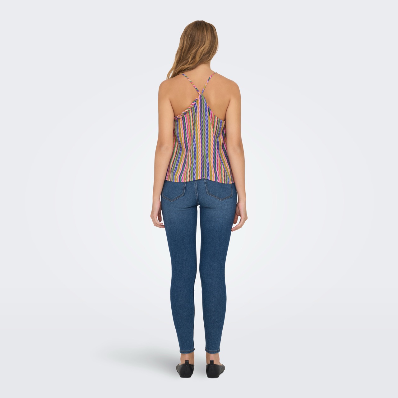 Mulher vista de costas com top colorido de riscas verticais e calças de ganga azul escuro.