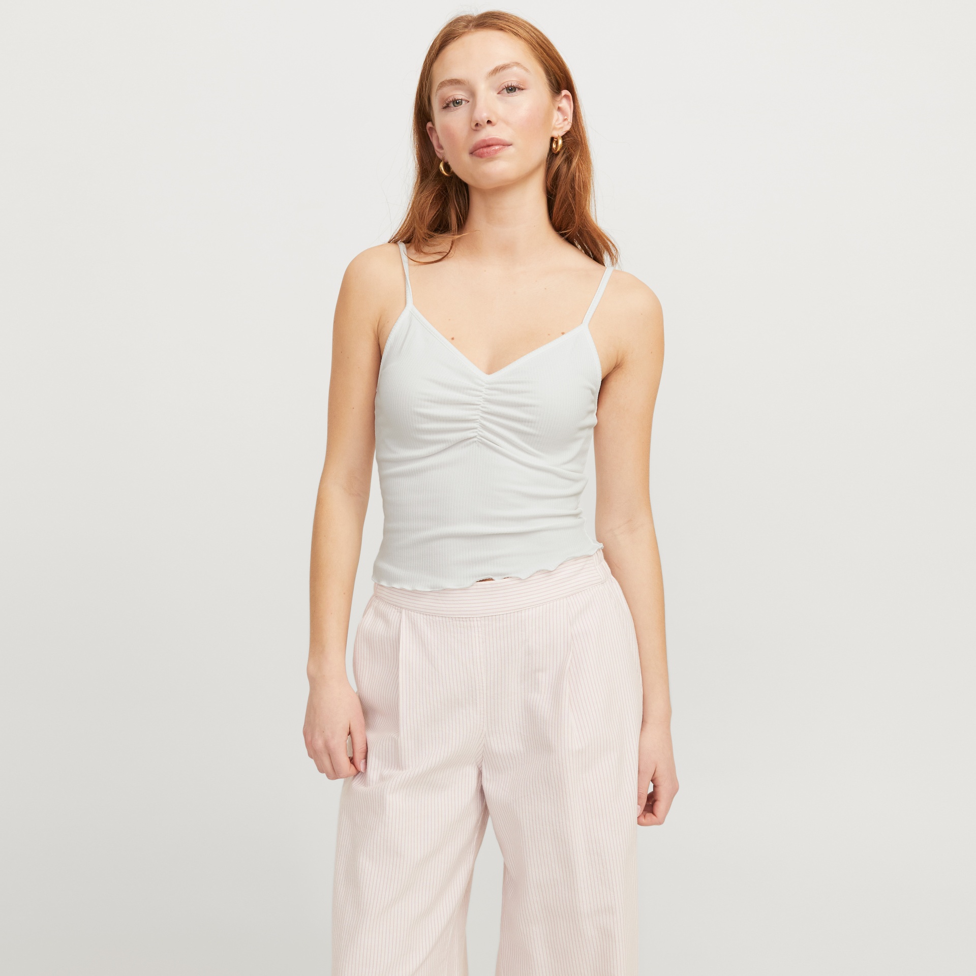 Mulher com top branco de alças finas e calças largas rosa claro com riscas.